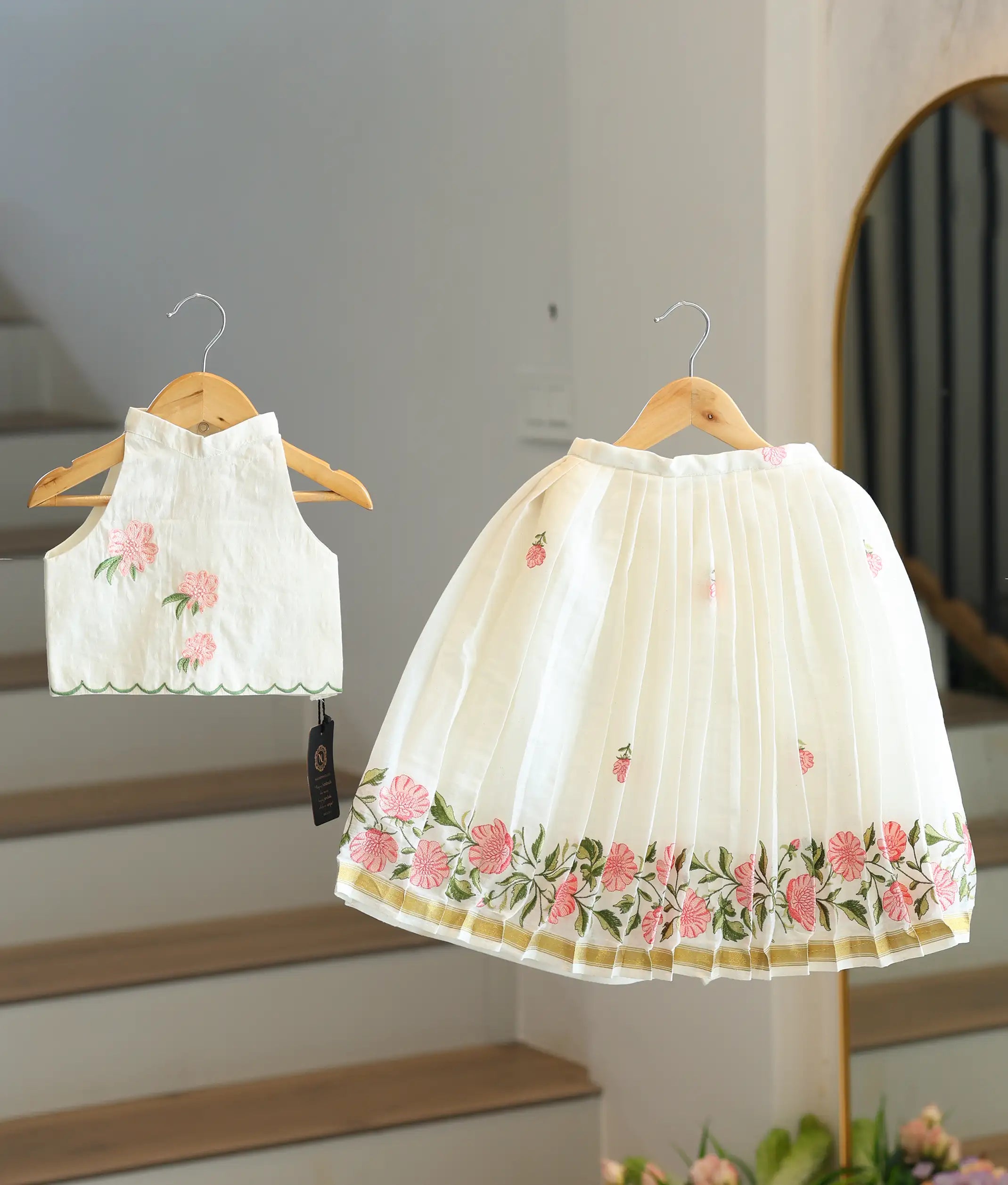 Front view of a girls' off-white skirt and top set with pink floral embroidery and a gold-bordered skirt.