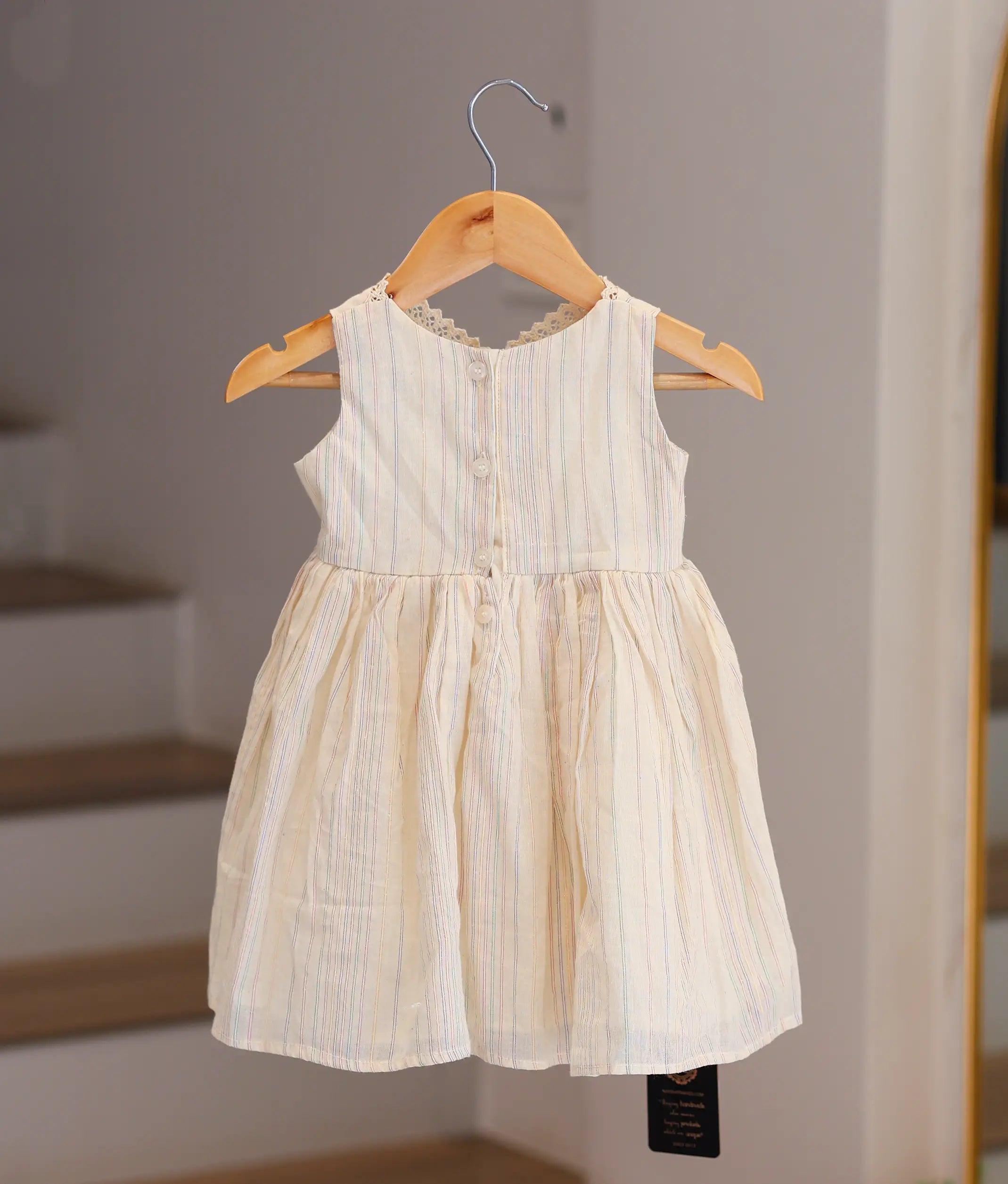 Back view of the off-white striped cotton frock showing the simple round neck and button closure