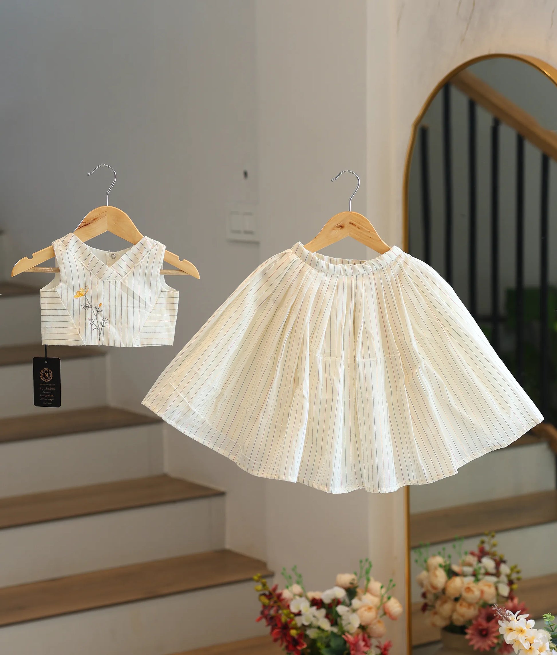 Front view of a girls' off-white skirt and top set with colorful stripes and floral embroidery.