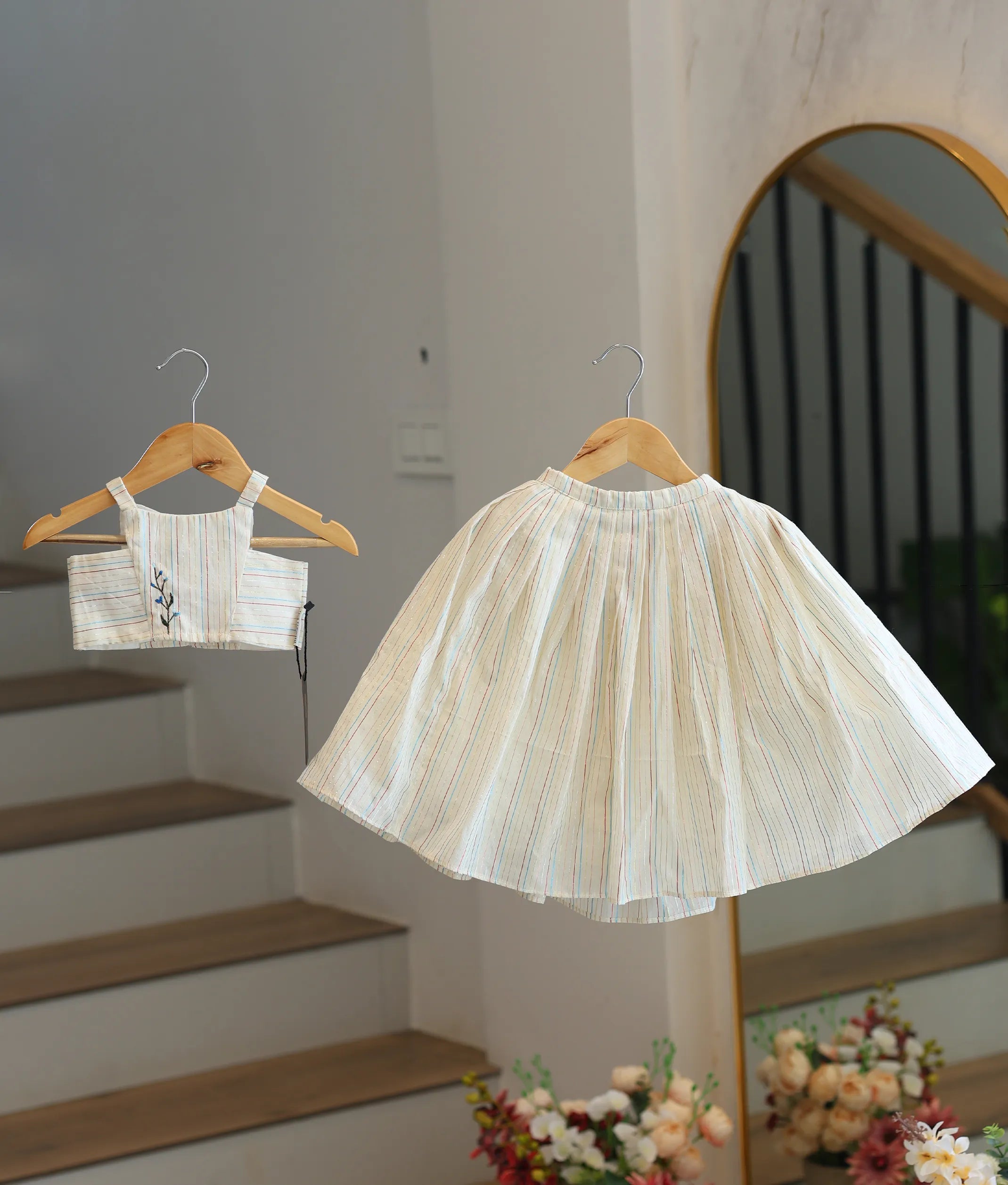 Front view of a girls' off-white skirt and top set with colorful stripes and floral embroidery.