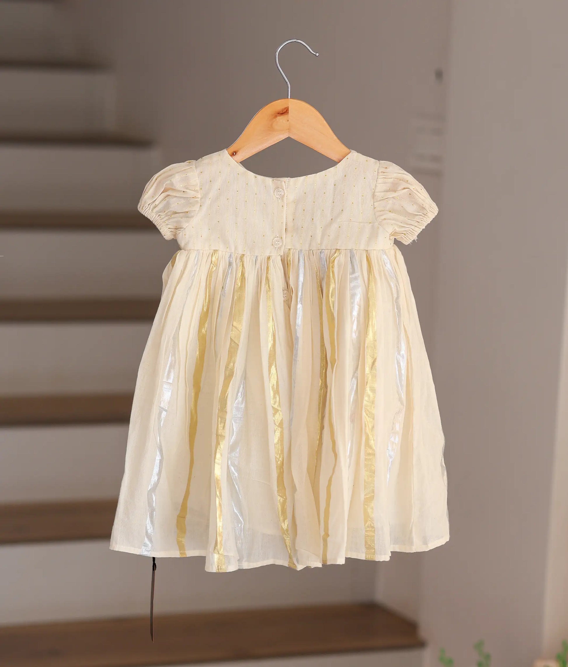 Back view of the off-white baby frock showing the gold and silver tissue stripes and simple button closure