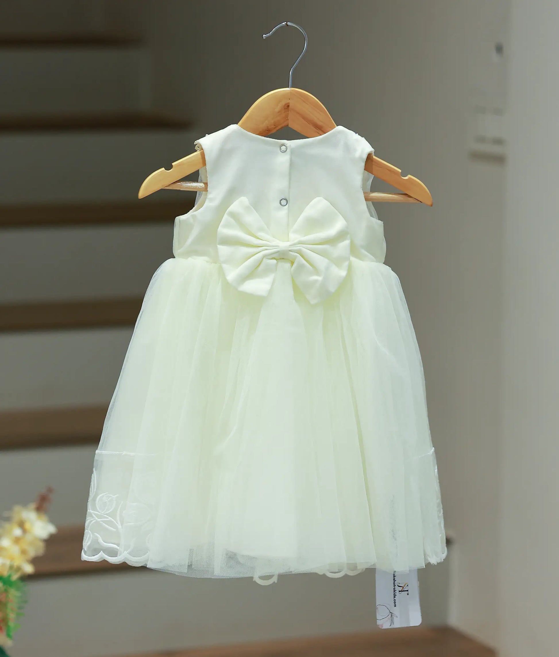 Back view of the off-white tulle net baptism frock highlighting the sleeveless design and the intricate floral embroidery on the scalloped skirt hem.
