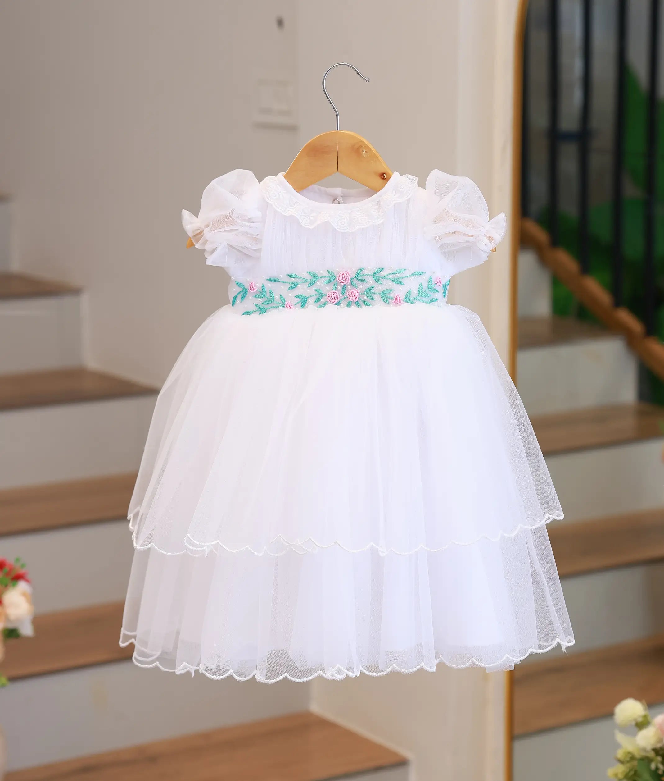 Full front view of an off-white tulle net baptism gown featuring a tiered skirt and hand-embroidered floral waistband.