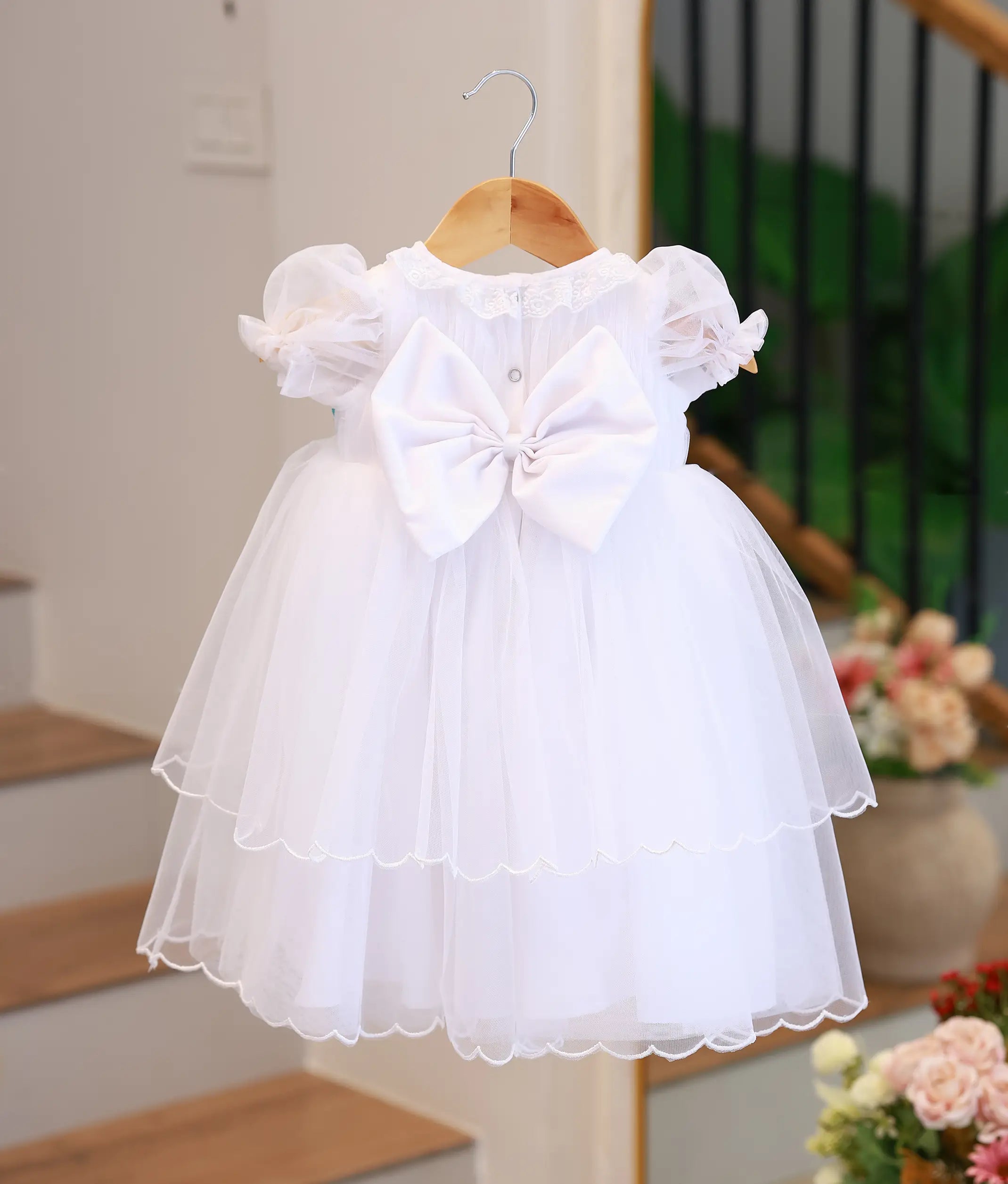 Back view of the off-white baptism gown highlighting the large satin statement bow and double-tiered tulle skirt.