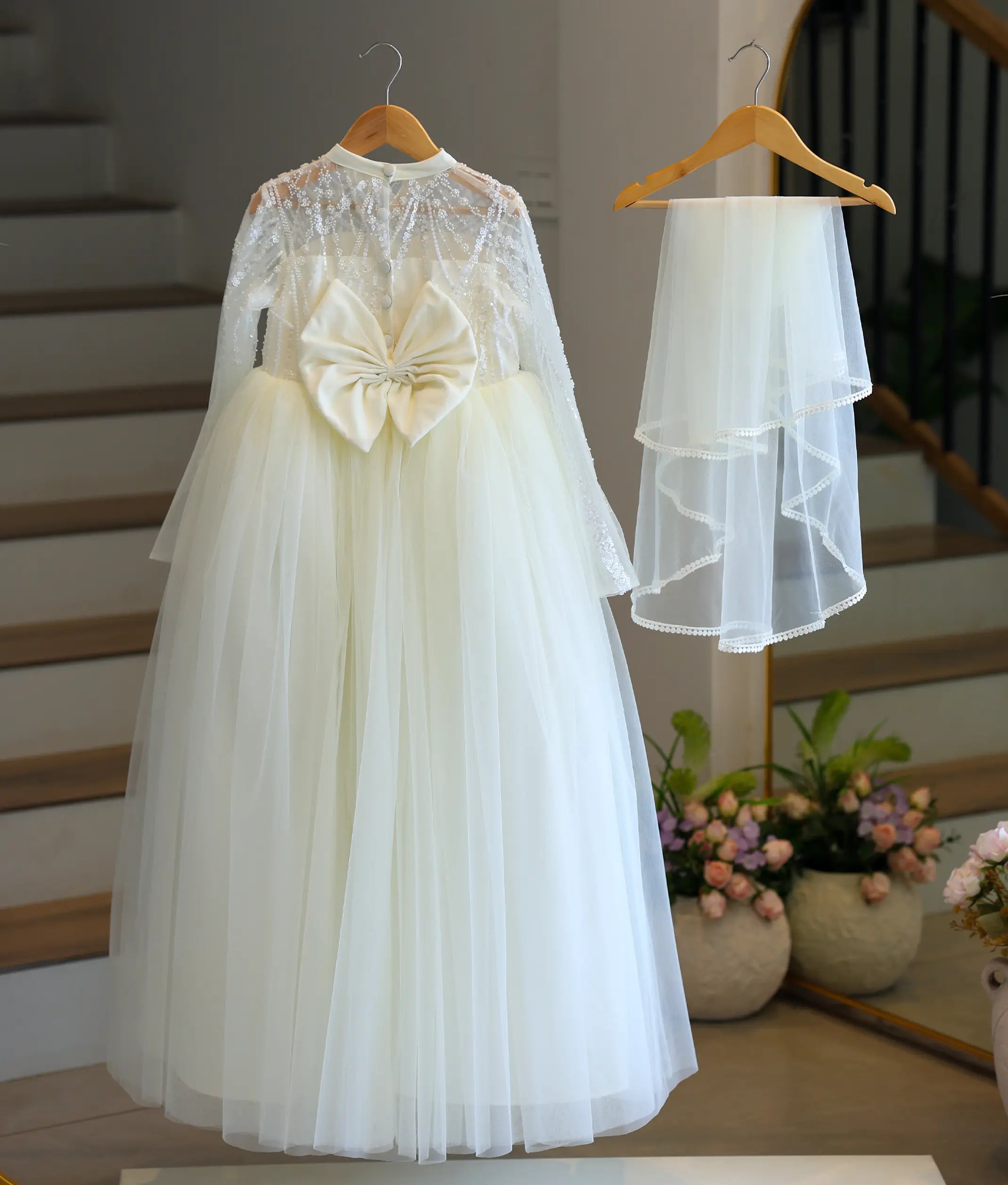 Back view of the off-white tulle net Holy Communion gown showing the high neck, elegant buttons, a large statement bow, and a matching layered veil with lace trim.
