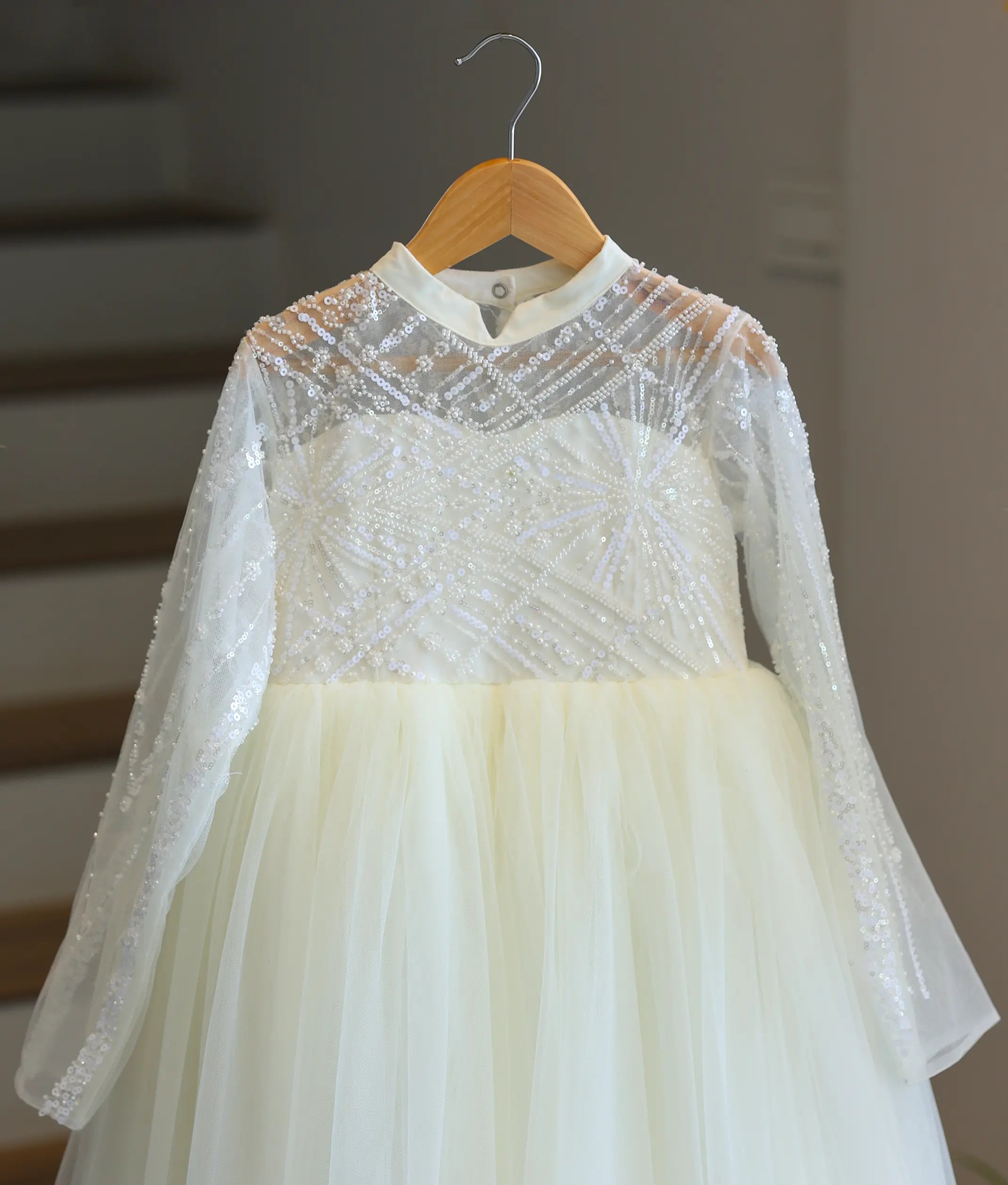 Close-up of the off-white Holy Communion dress bodice, showing the geometric patterns of the shimmering sequin work material, high collar, and sheer long sleeves.