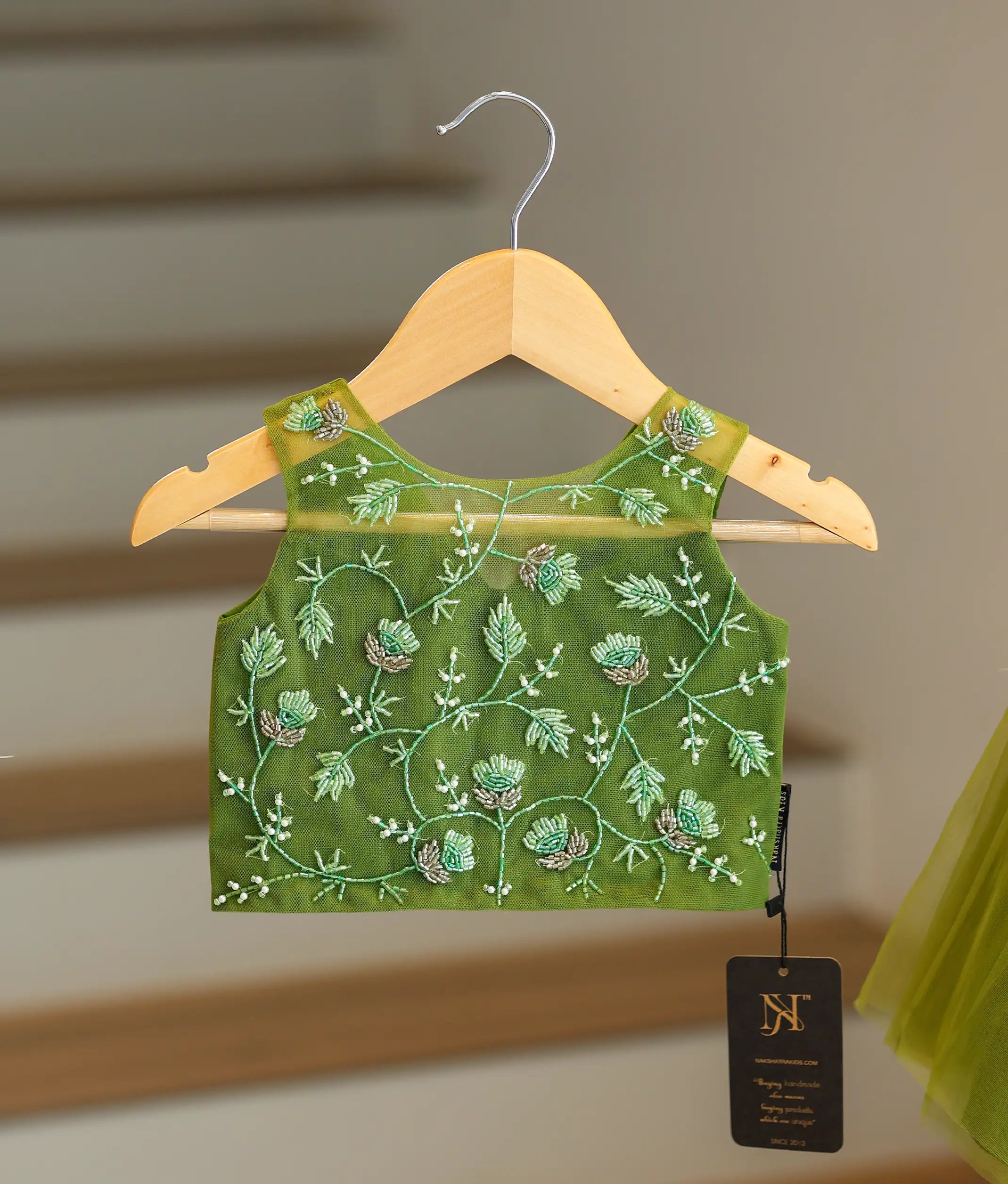 Close-up of the white floral embroidery, pearls, and silver beads on the olive green top
