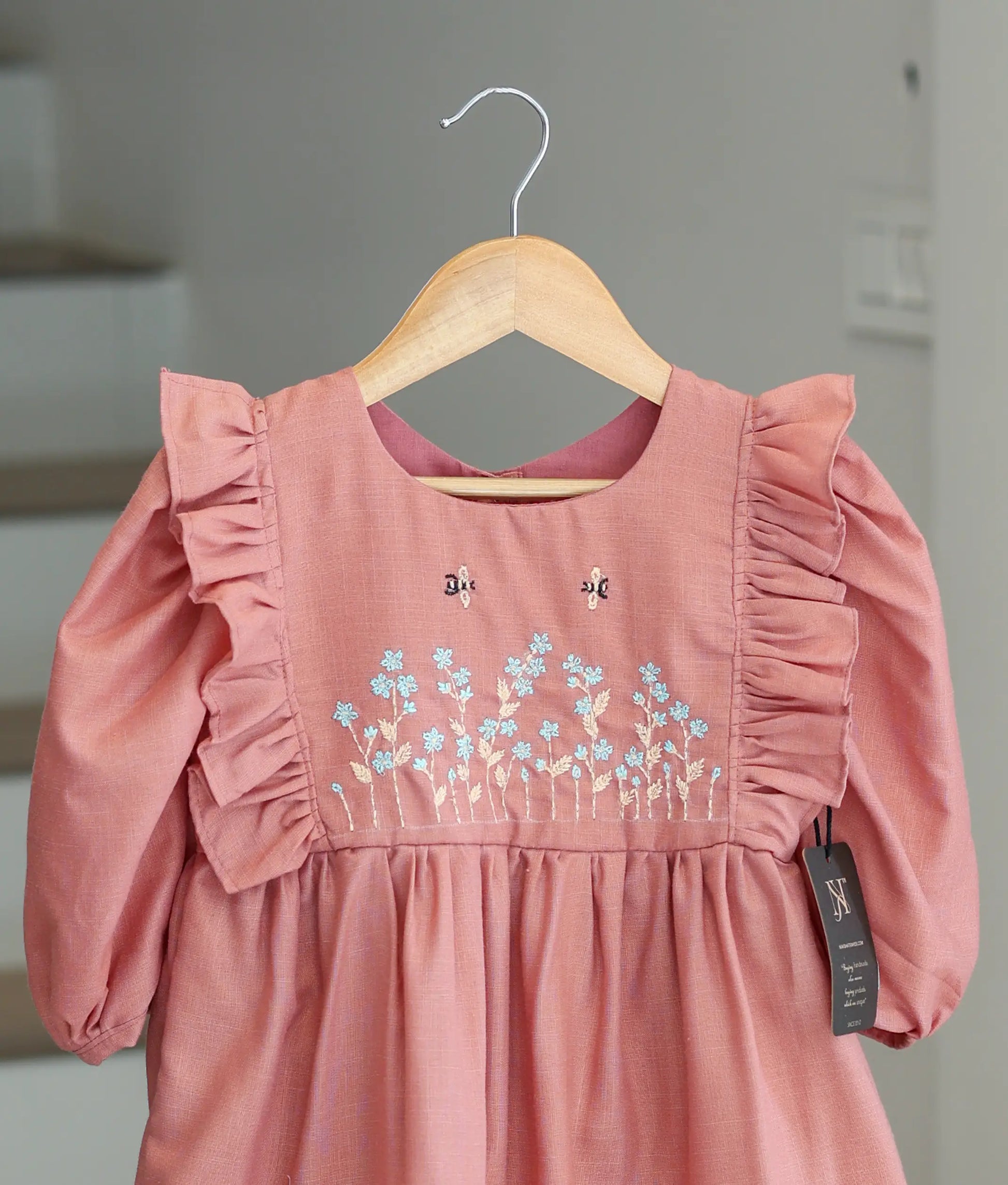 Close-up of the cotton dress showing the detailed handmade floral embroidery and pearl accents