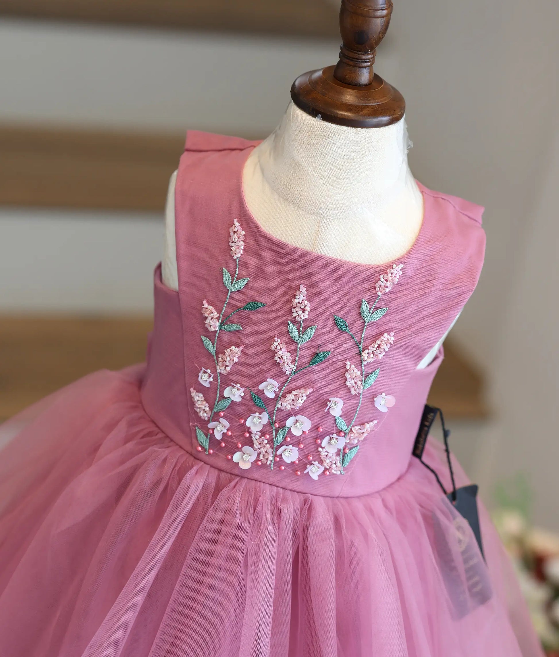 Close-up view of the intricate floral hand embroidery, beadwork, and V-shaped panel on the yoke of an onion-pink girls' frock.
