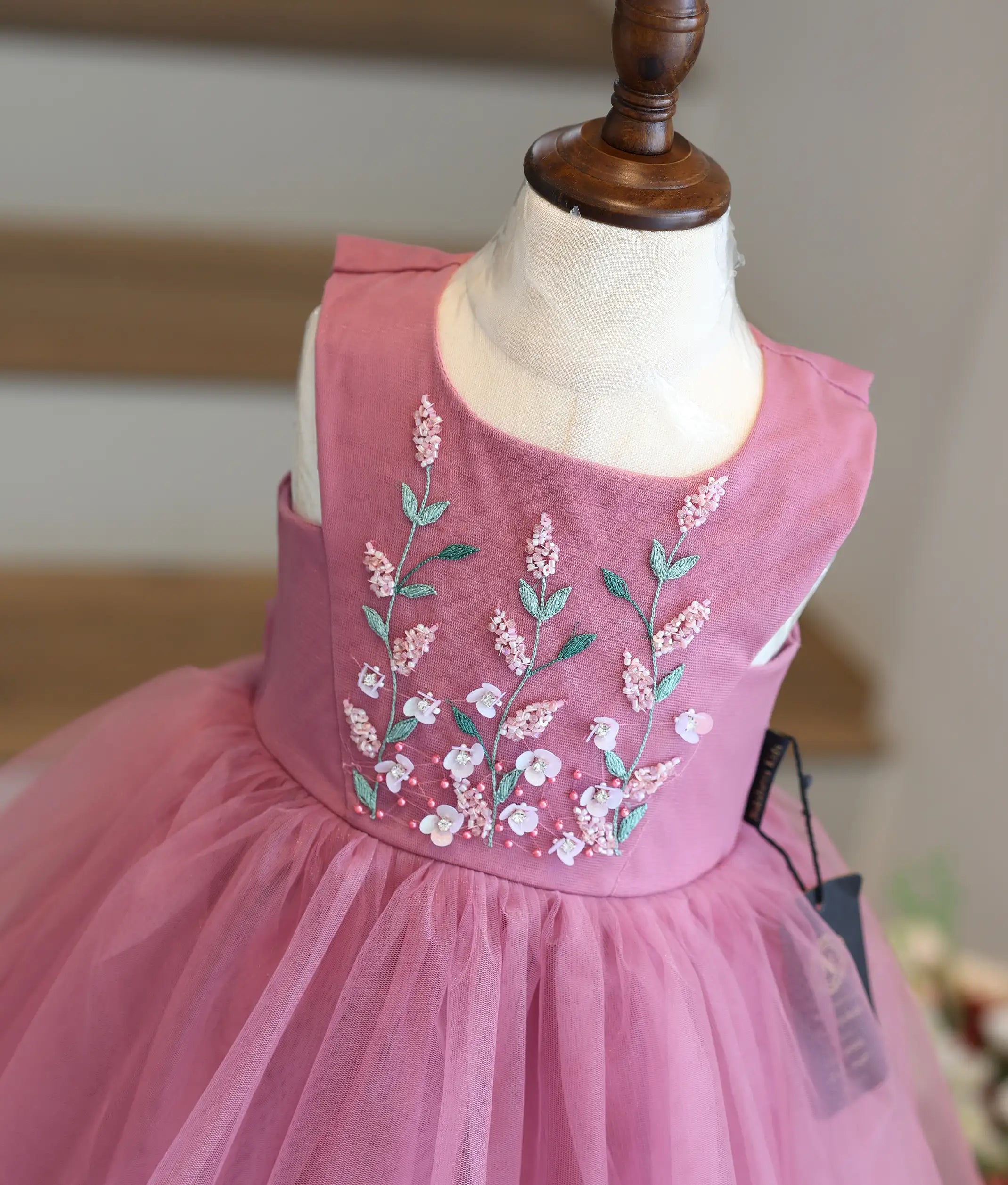Close-up view of the intricate floral hand embroidery, beadwork, and V-shaped panel on the yoke of an onion-pink girls' frock.