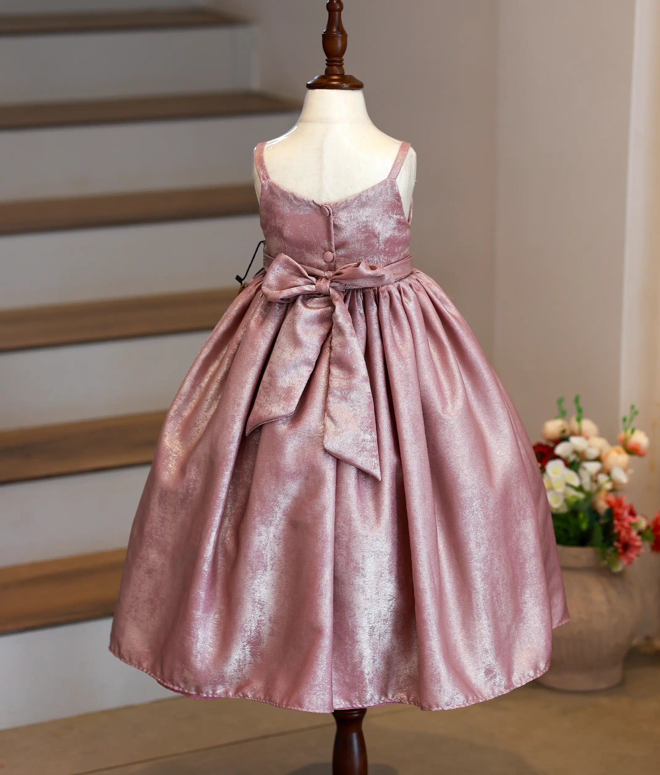 Back view of onion pink milan foil gown showing the wide neckline, show button, and the elegant bow with tie closure