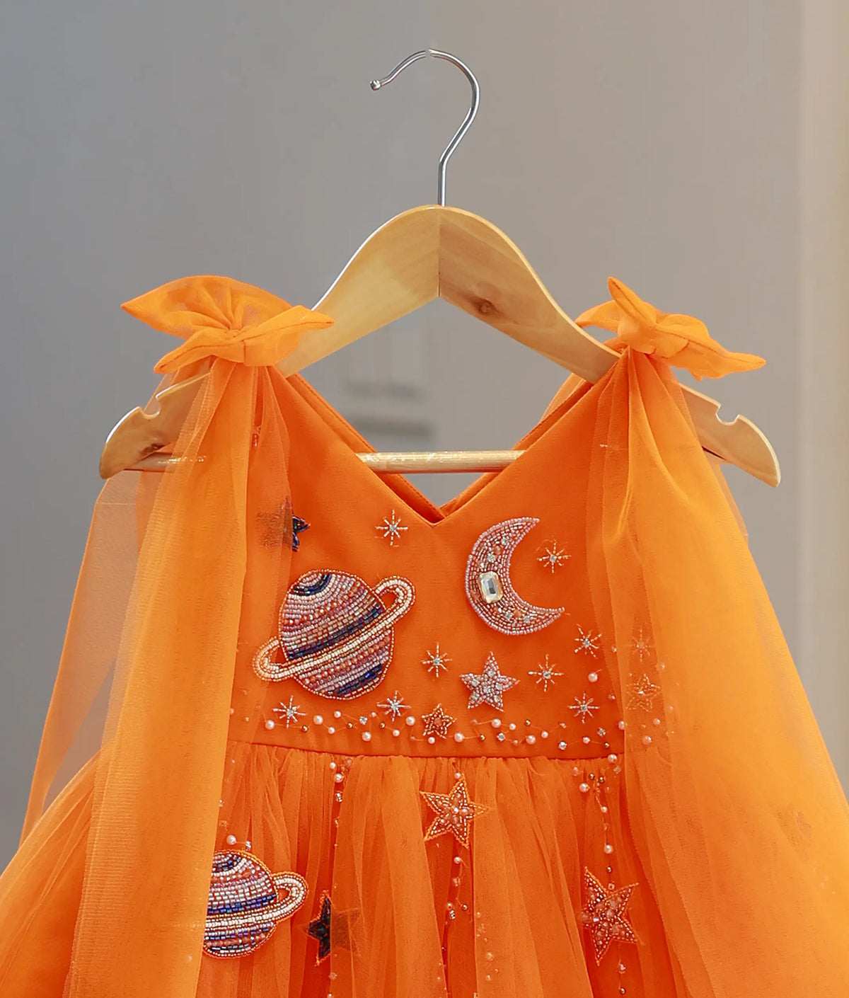 Close-up view of orange frock top showing beaded planet Saturn, crescent moon, and star handwork.