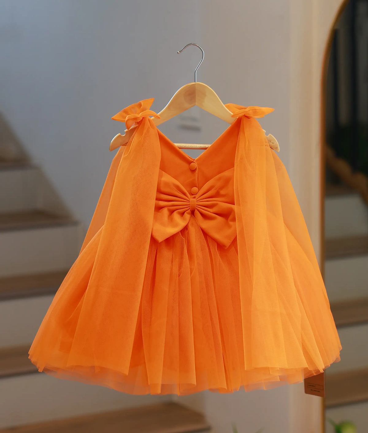 Back view of a bright orange galaxy theme frock showing V-back with buttons and waist bow.