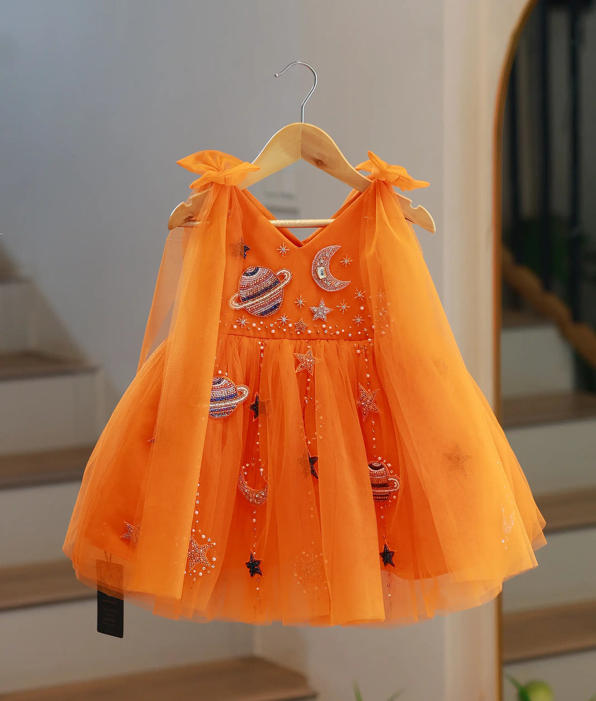Front view of bright orange galaxy theme handwork tulle net baby girl frock on hanger.