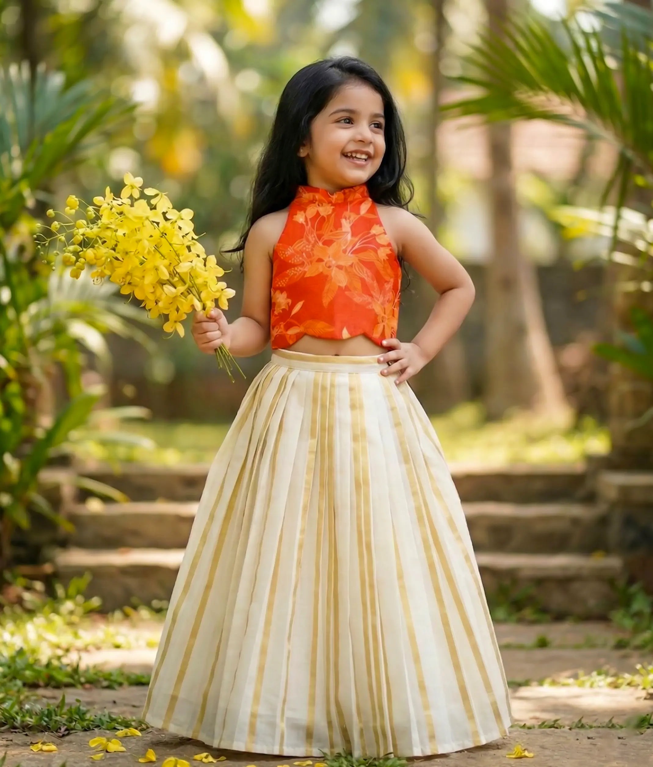 Baby girl wearing an ethnic orange floral silk top with a kasavu-striped skirt.