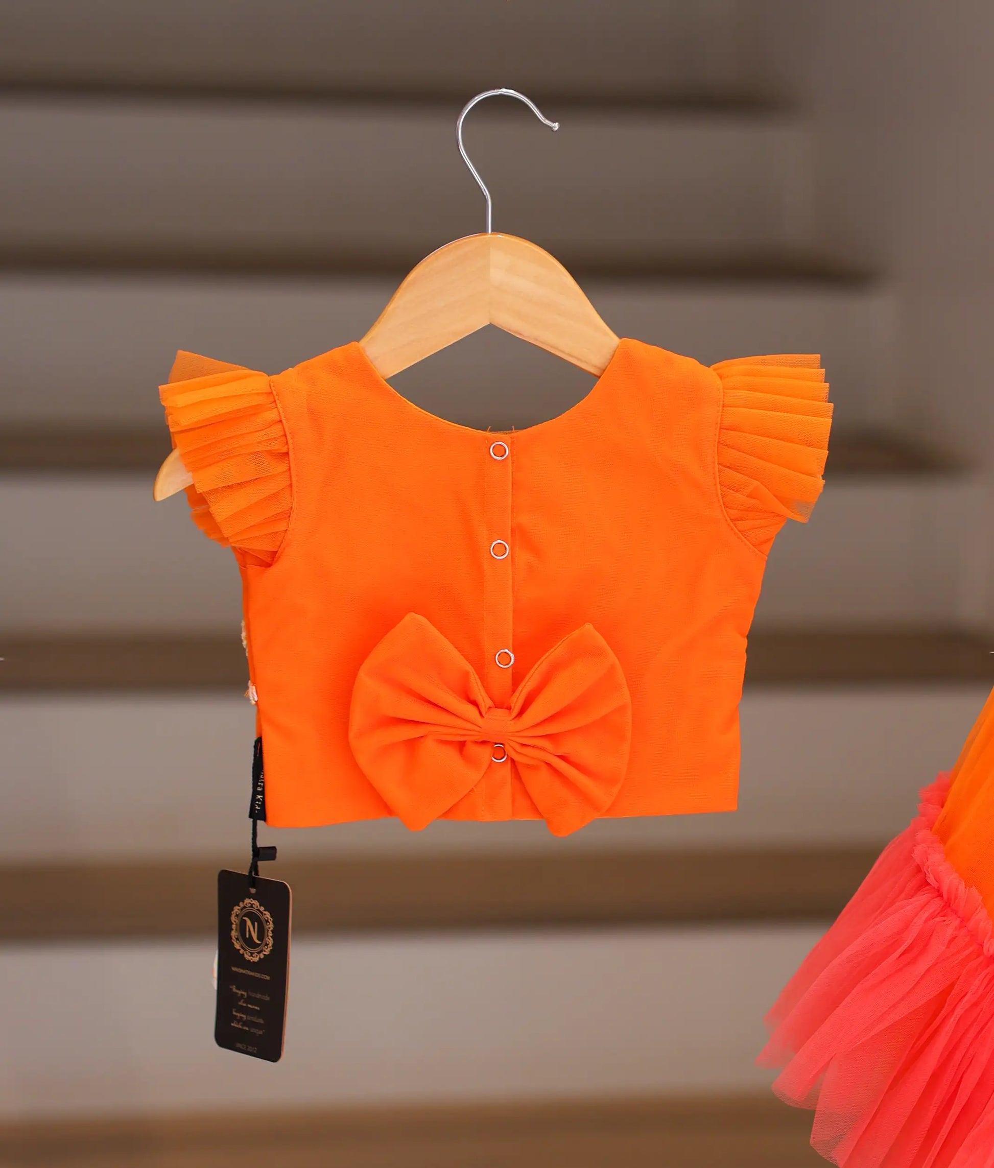 Back view of the orange crop top and skirt showing the round neck, button closure, and decorative bow