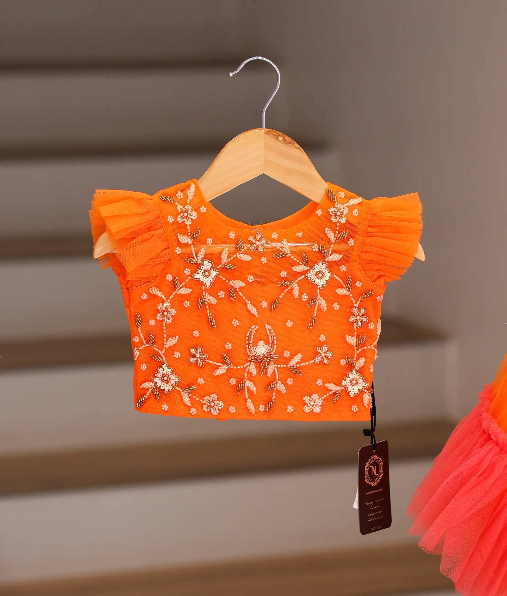 Close-up of the intricate floral embroidery and ruffled sleeves on the orange crop top