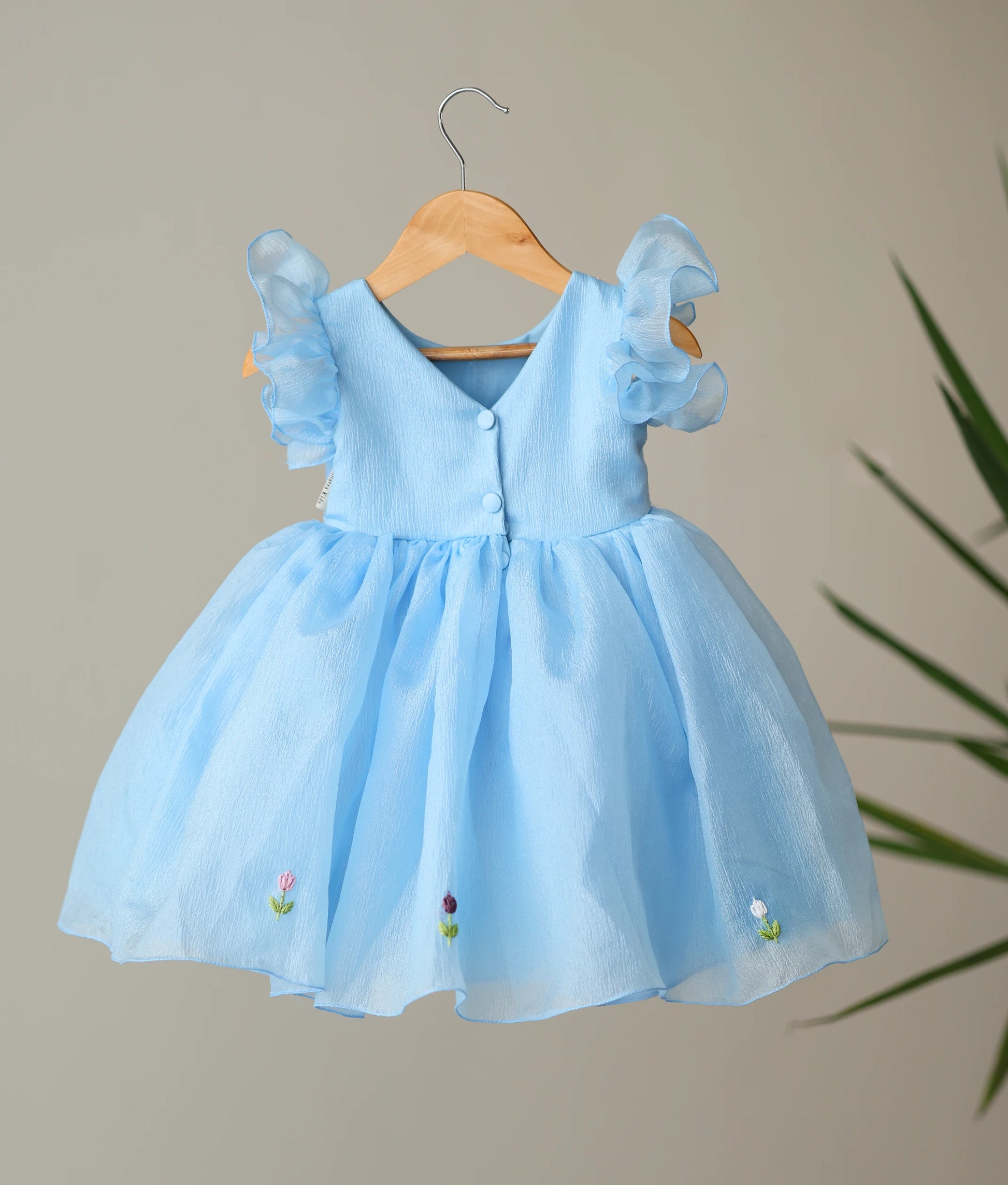Back view of pastel blue crush organza dress showing the elegant V-neckline with show button and the multiple-layered flared skirt