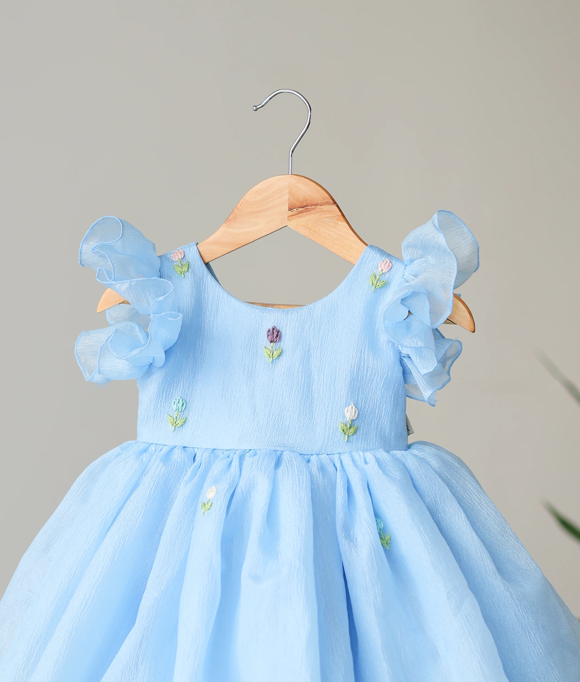 Close-up of the charming multicolor floral handwork on the yoke and butterfly sleeves of the pastel blue birthday dress