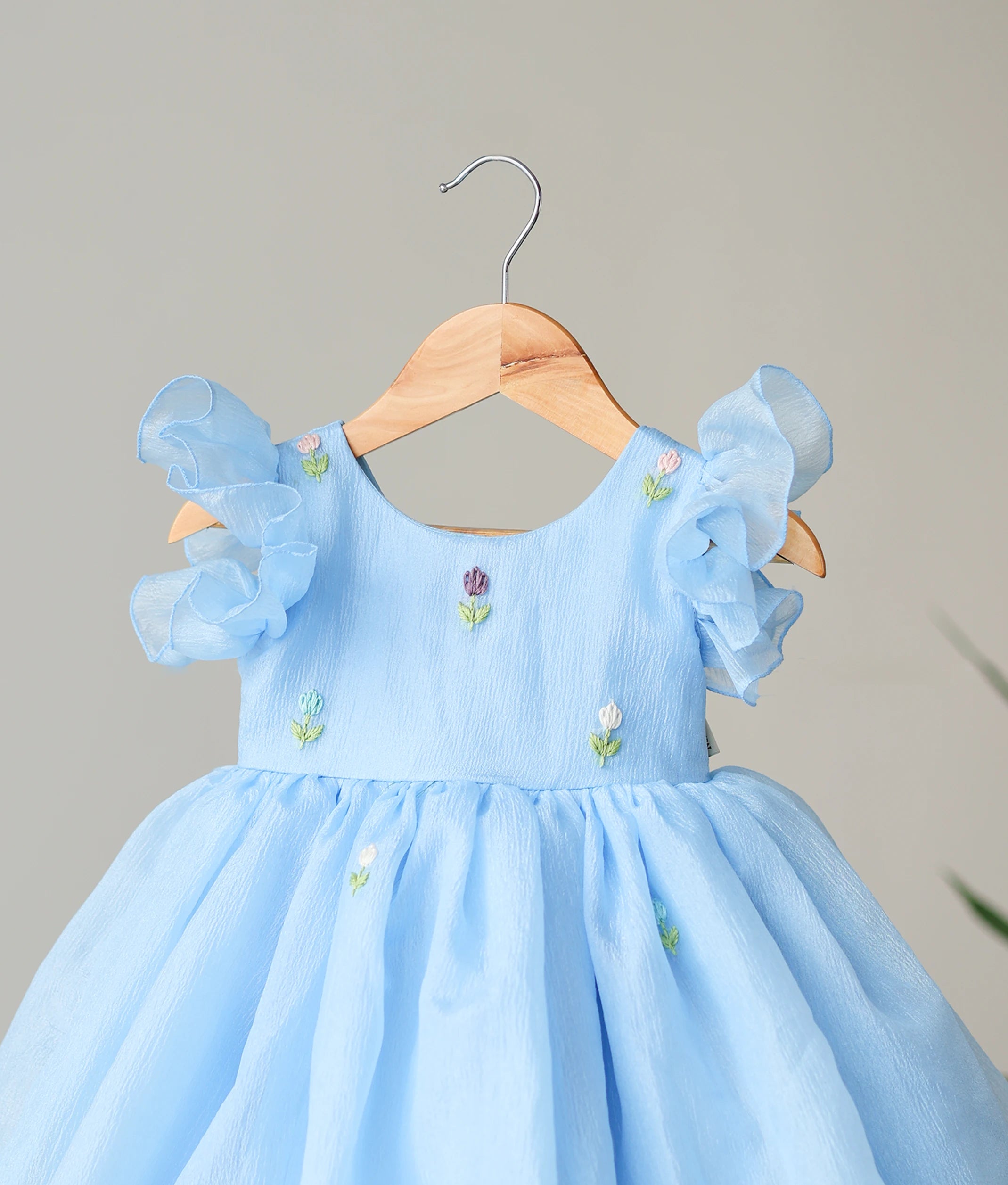 Close-up of the charming multicolor floral handwork on the yoke and butterfly sleeves of the pastel blue birthday dress