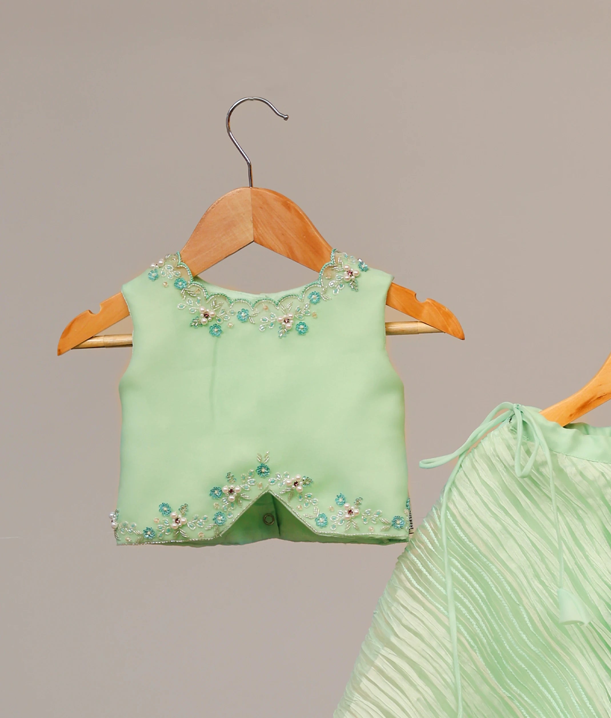 Close up of sparkling floral beadwork and sequin detailing on the pastel green handworked top