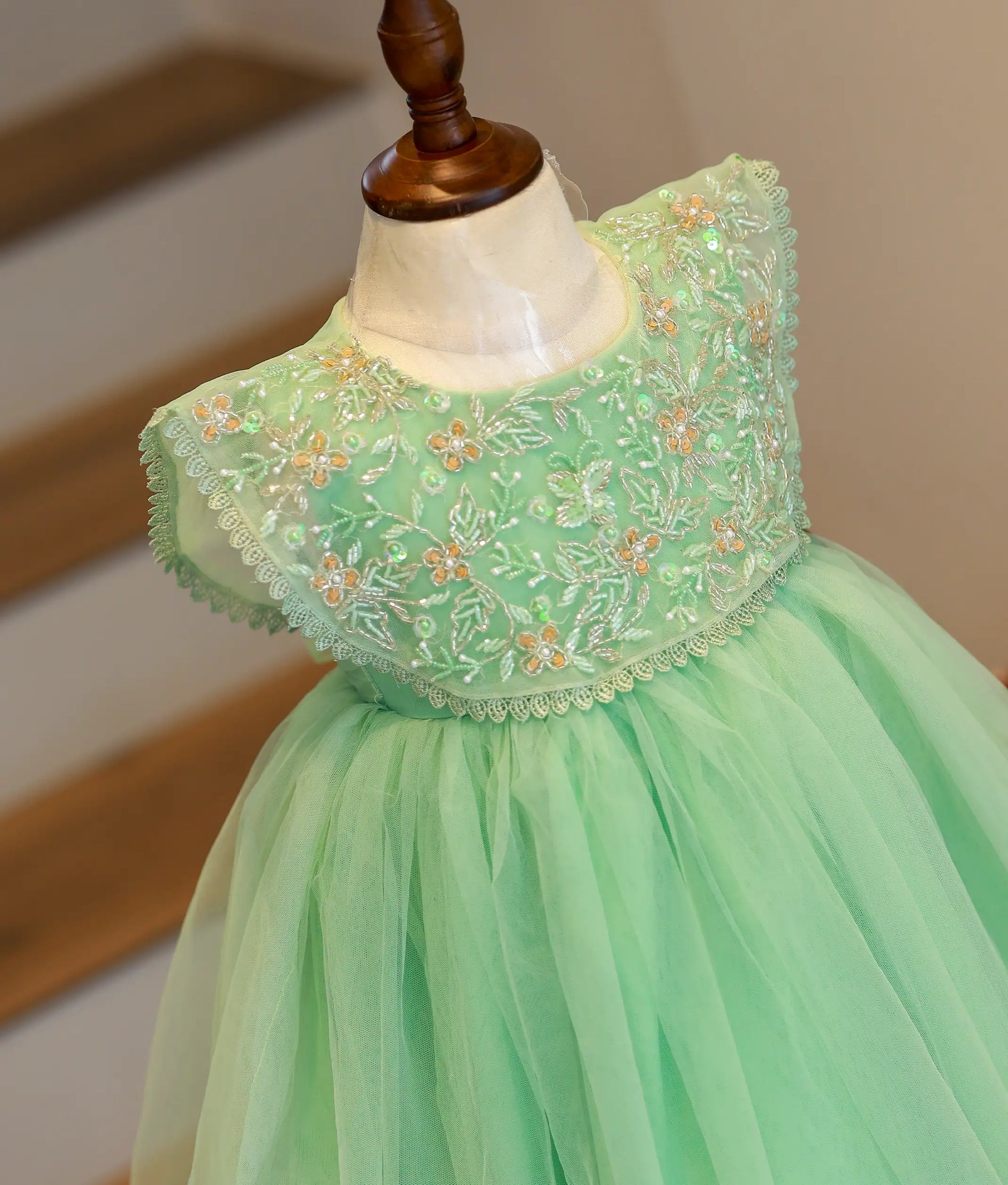 Close-up of the pastel green frock highlighting the intricate floral beadwork and sequins on the scalloped cape.