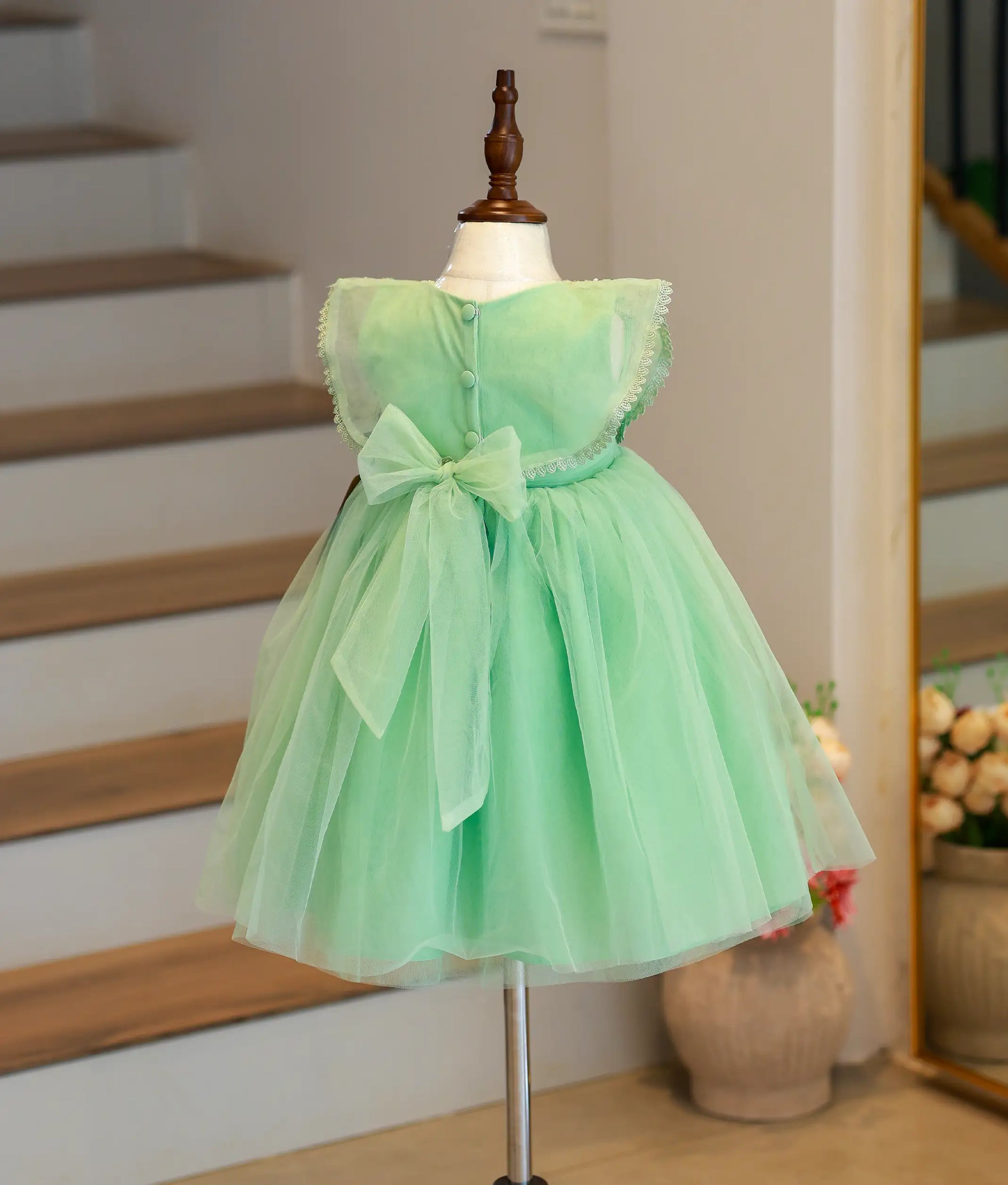 Back view of the pastel green party frock showing the button closure and the large sheer tulle statement bow.