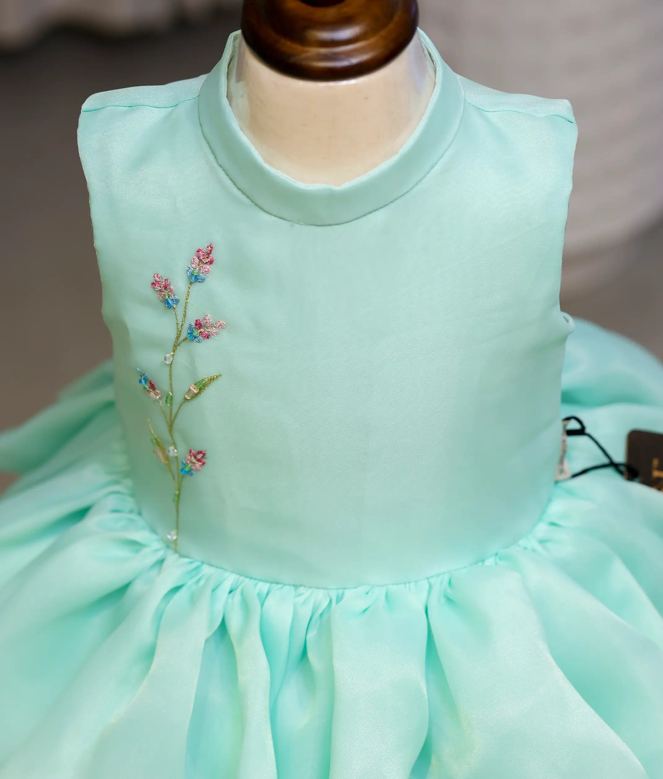 Close-up of the delicate multi-colored floral handwork on the halter-neck yoke of the pastel green organza birthday dress
