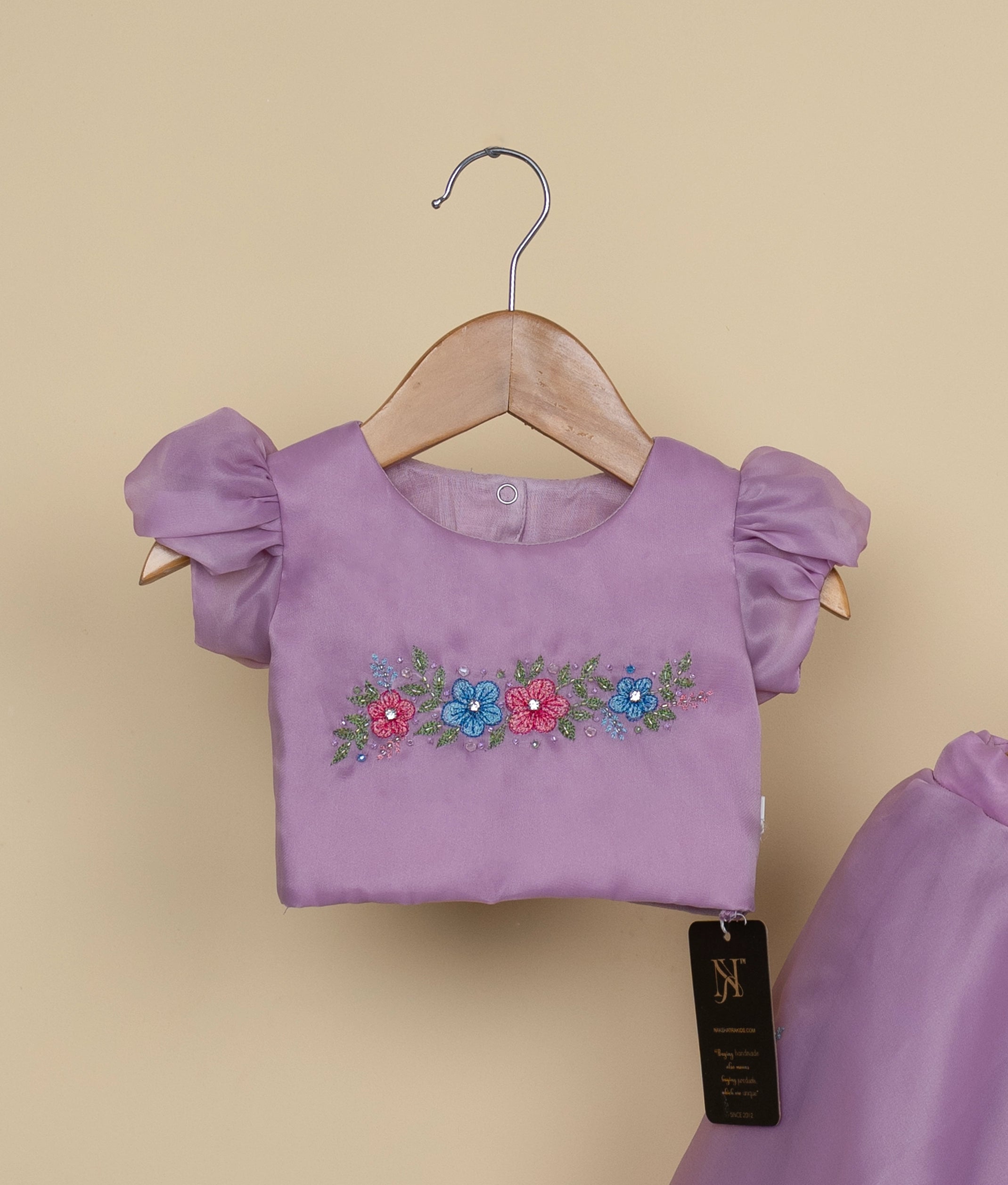 Close-up of the pastel lavender crop top showing the horizontal floral embroidery, hand-work, and puffed sleeves