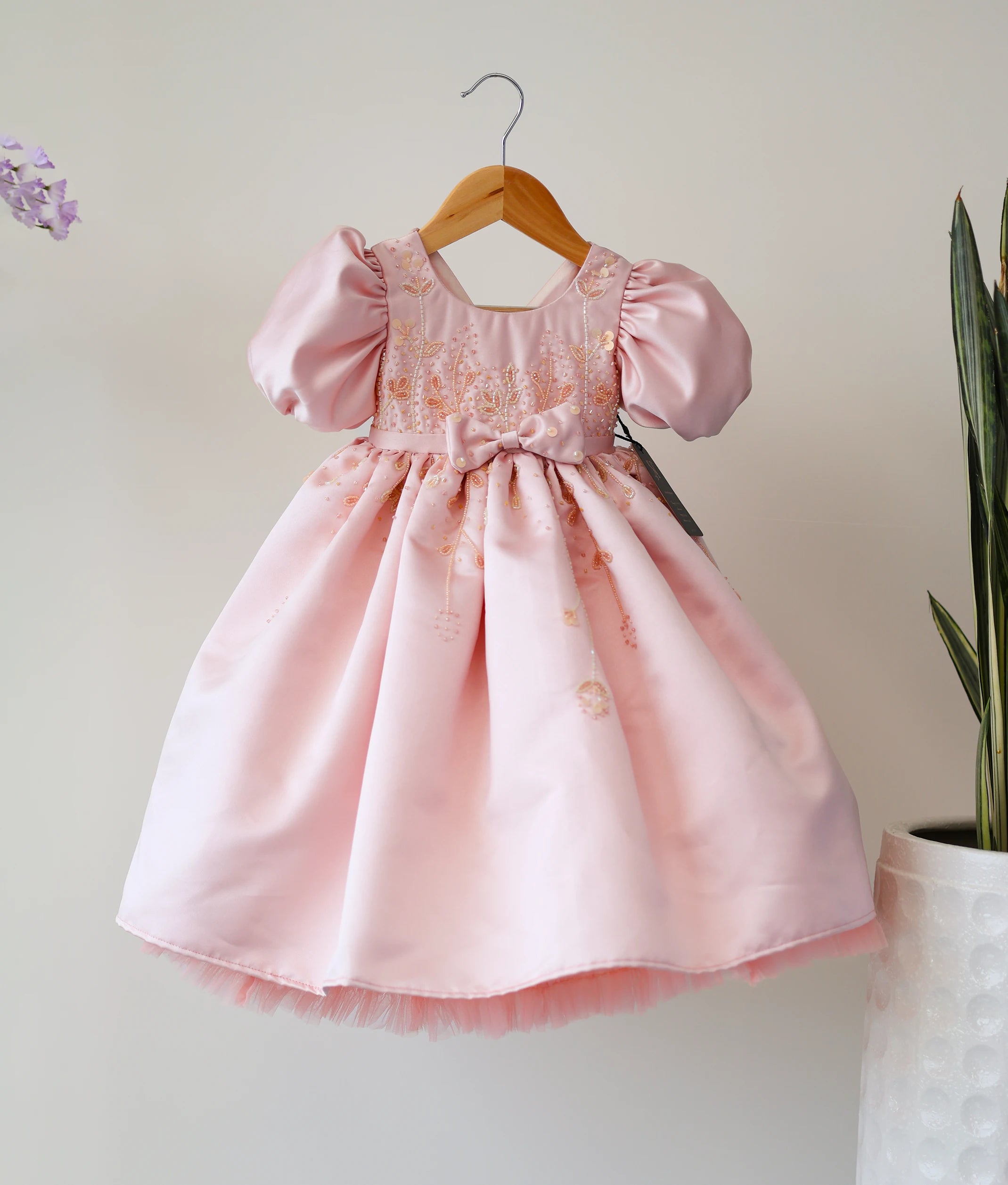 Front view of a pastel peach bridal satin birthday gown for baby girls with cut-bead handwork and balloon sleeves