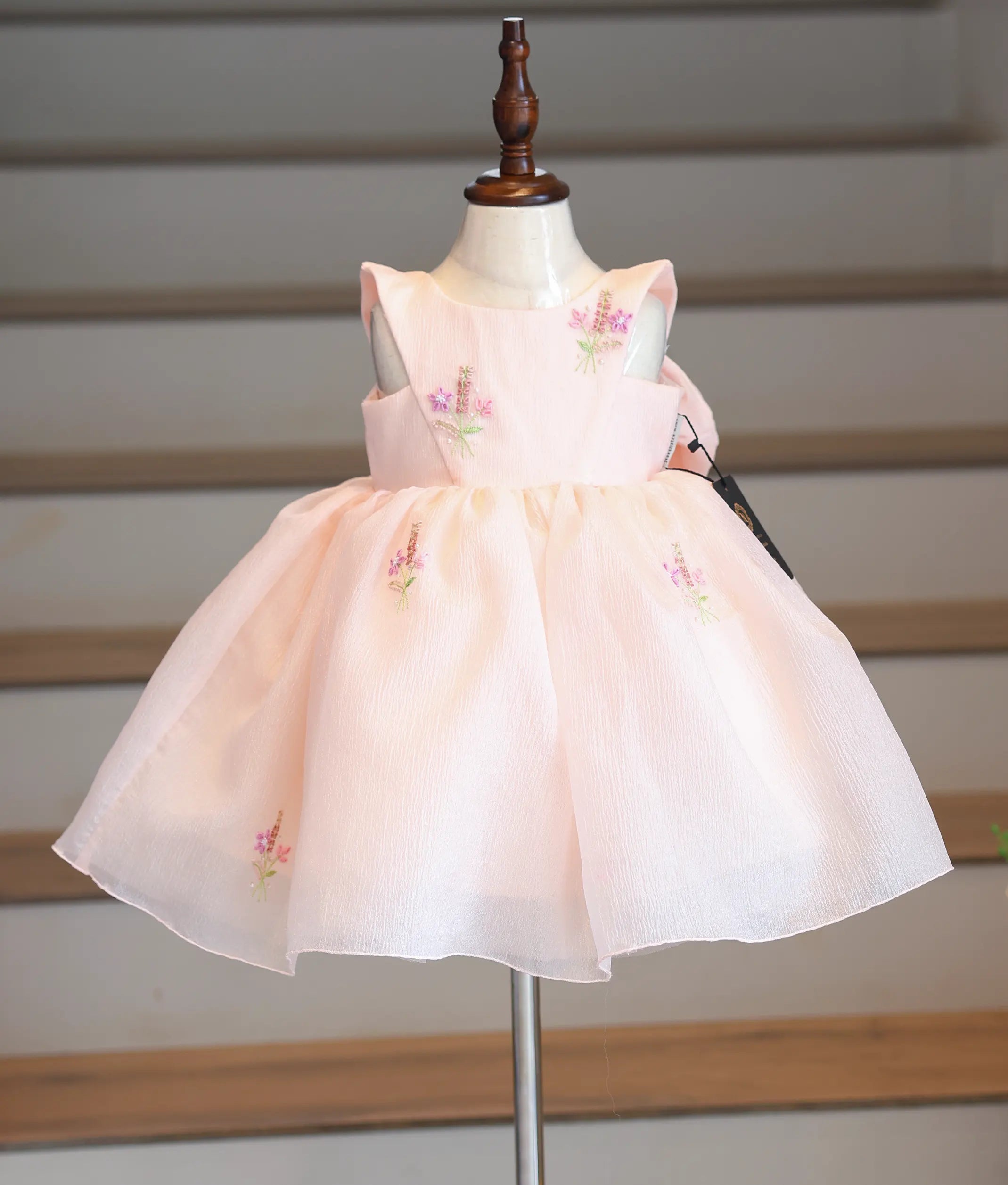 Front view of a pastel peach crush organza frock with floral handwork and V-shaped overlay.