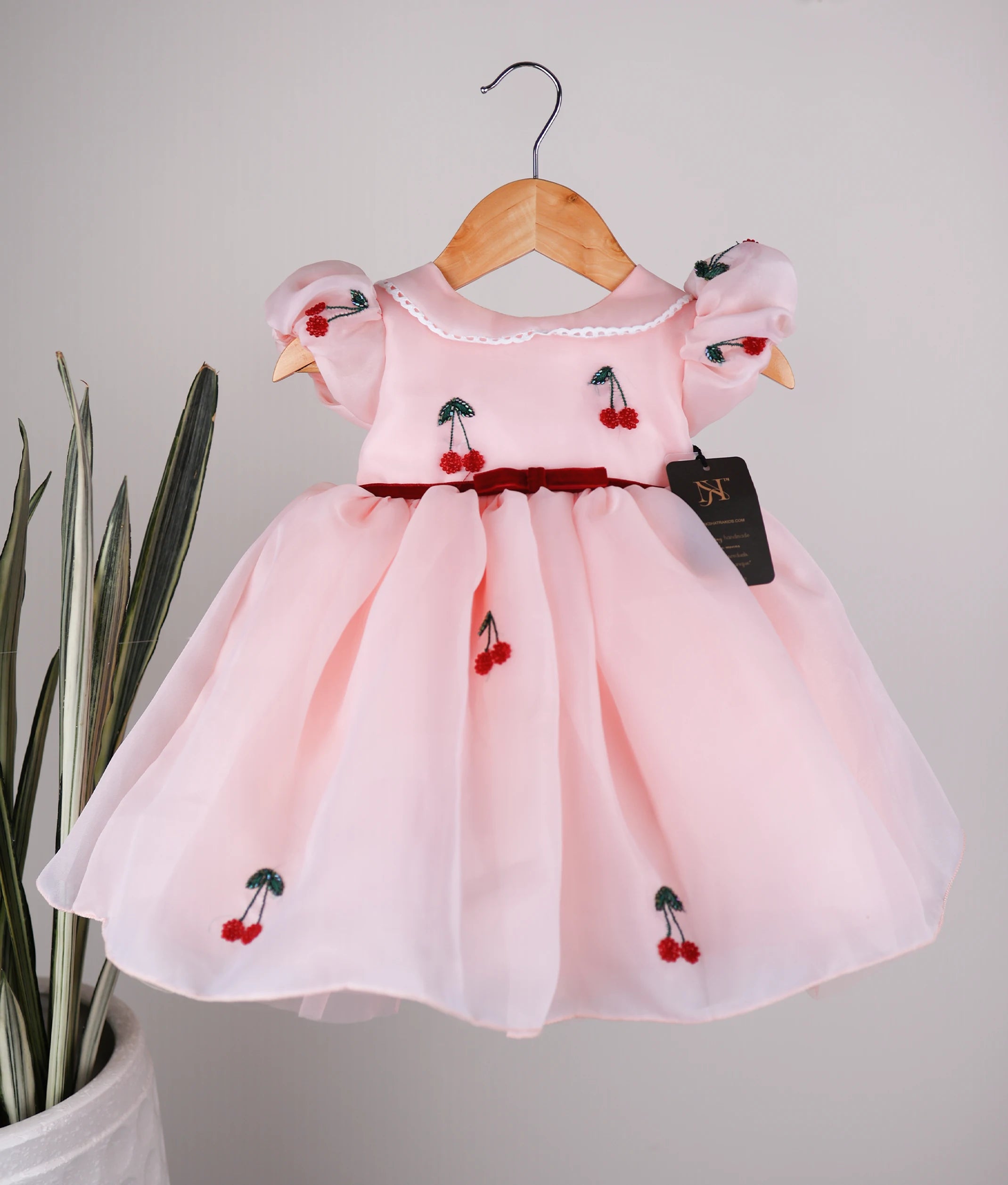 Front view of a pastel peach organza girl's dress with cherry motifs, Peter Pan collar, and puffed sleeves
