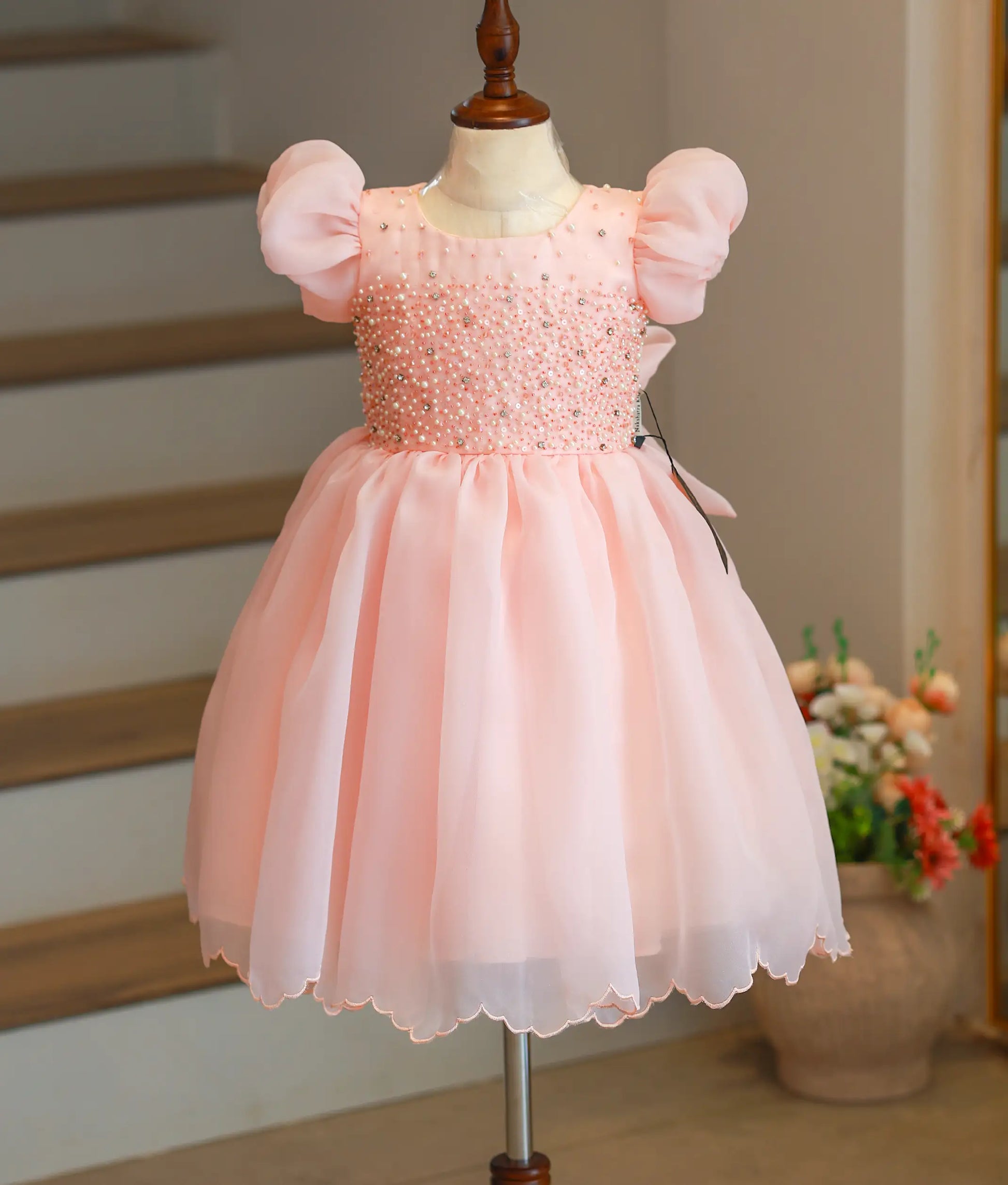 Front view of a pastel peach handworked organza birthday frock for baby girls with puff sleeves and a flared skirt