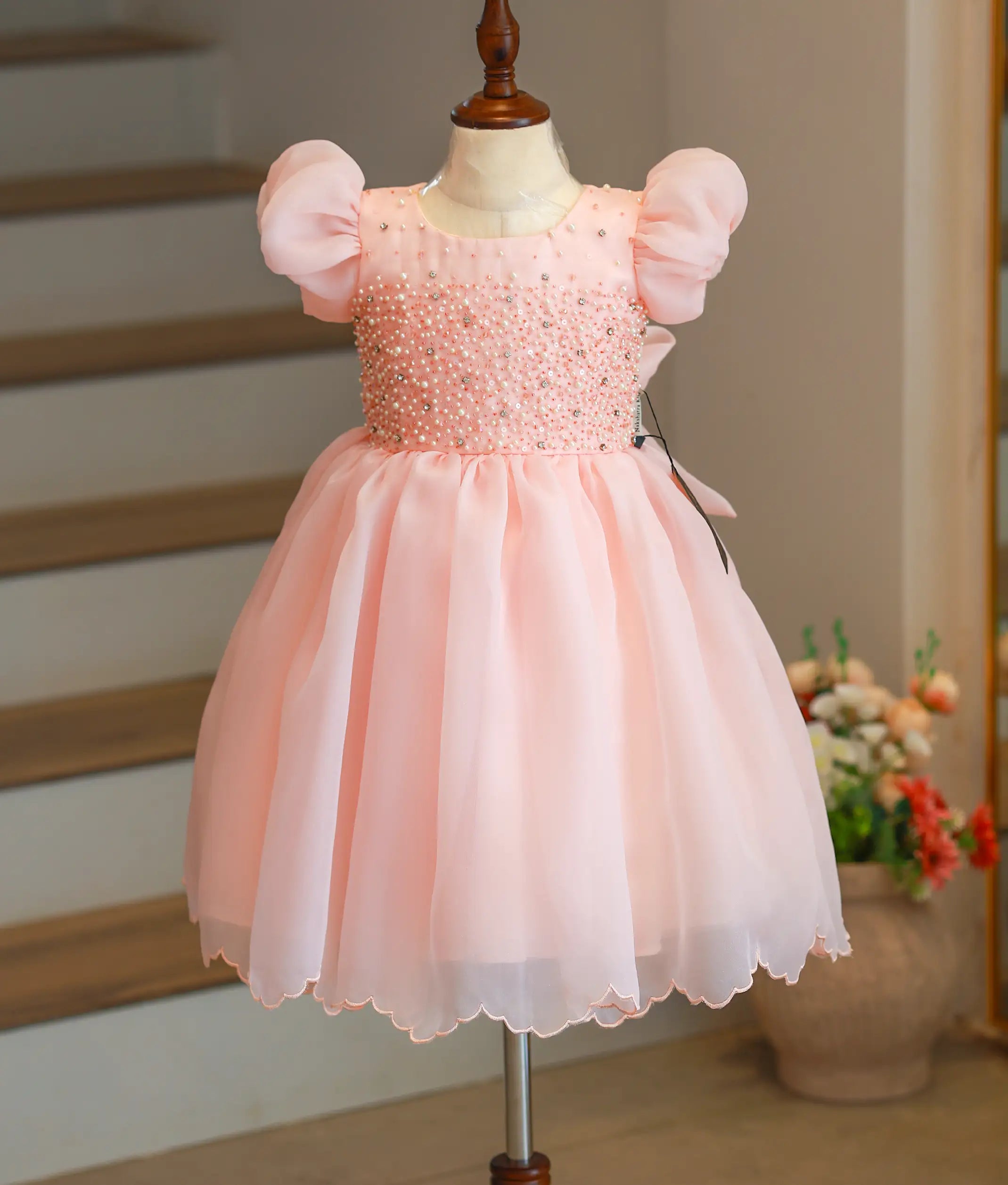 Front view of a pastel peach handworked organza birthday frock for baby girls with puff sleeves and a flared skirt