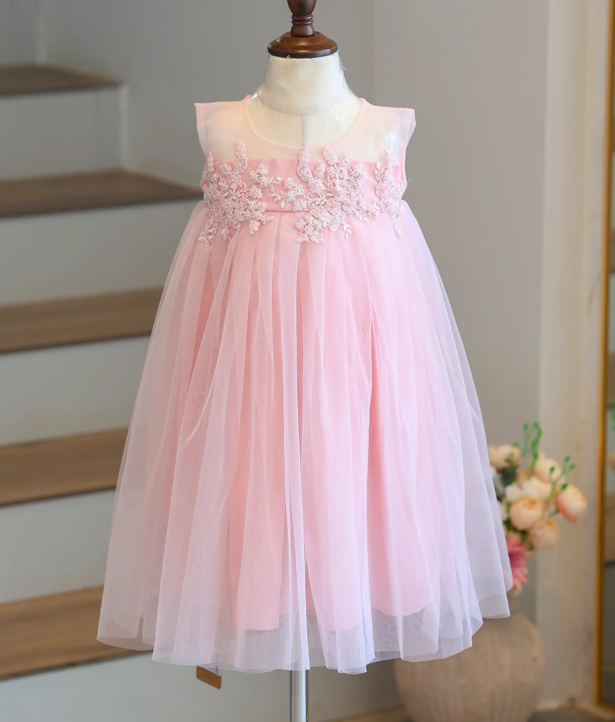 Front view of a pastel pink girls' frock with applique work and a pleated tulle bottom.