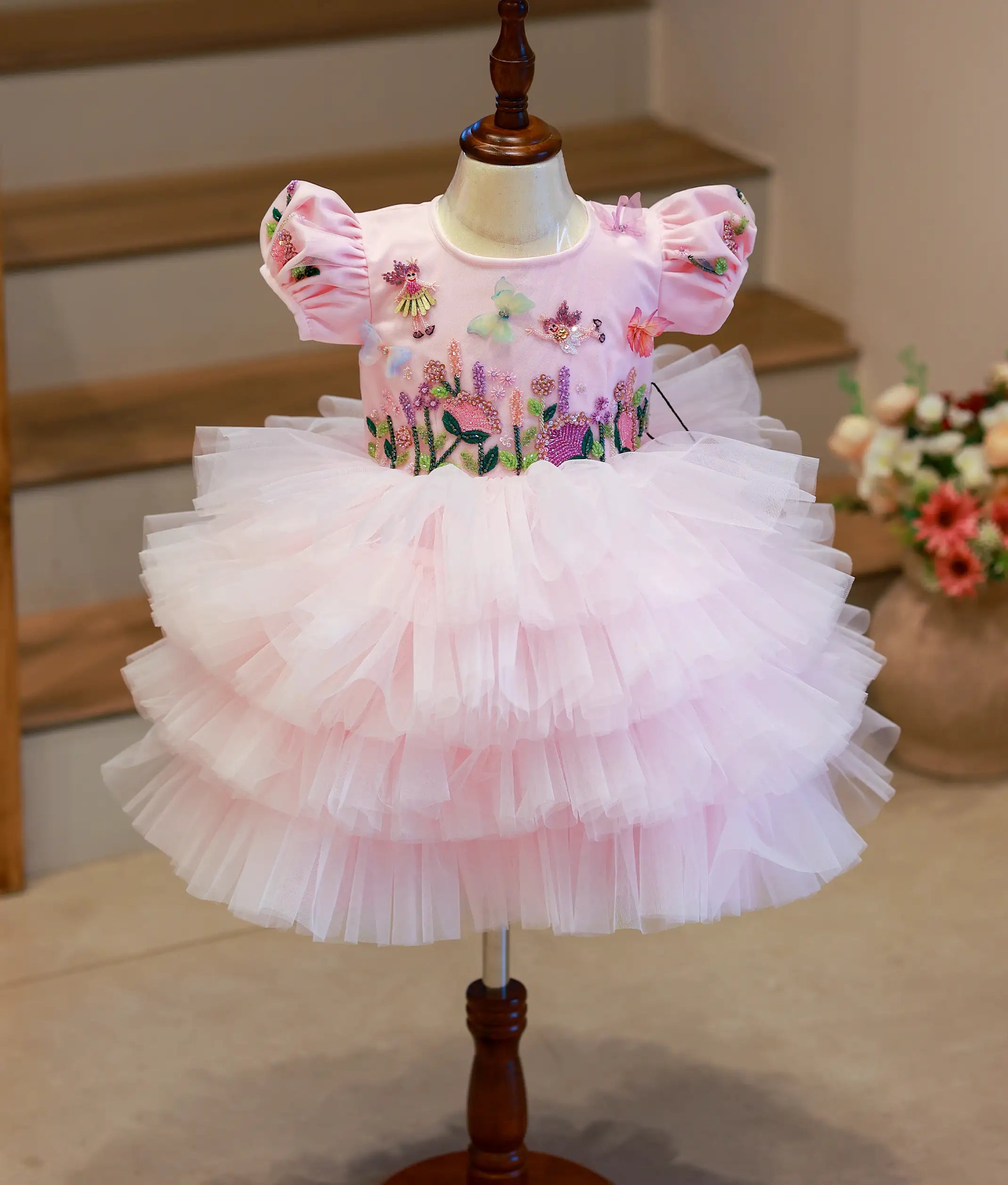 Front view of a pastel pink fairy-themed birthday frock with handworked butterfly motifs and a step-pattern tulle flare.