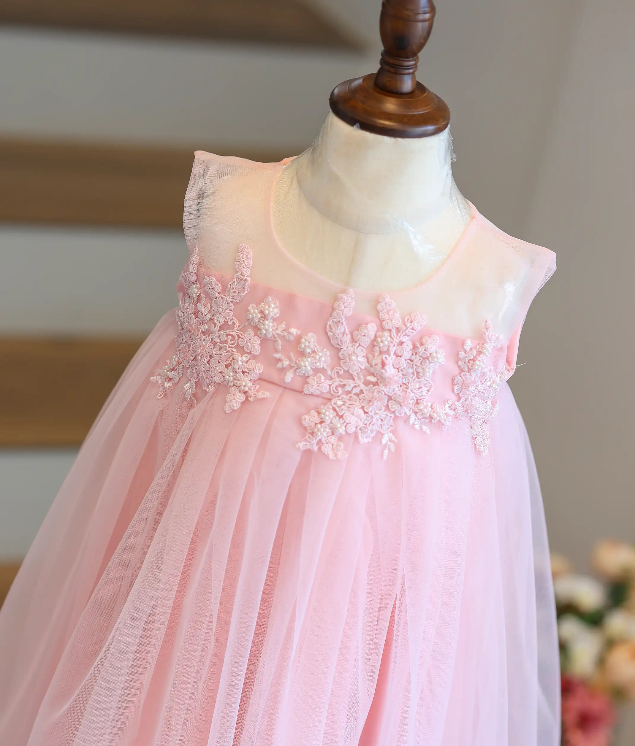 Close-up of the pastel pink frock showing the transparent net top and applique work detailing.