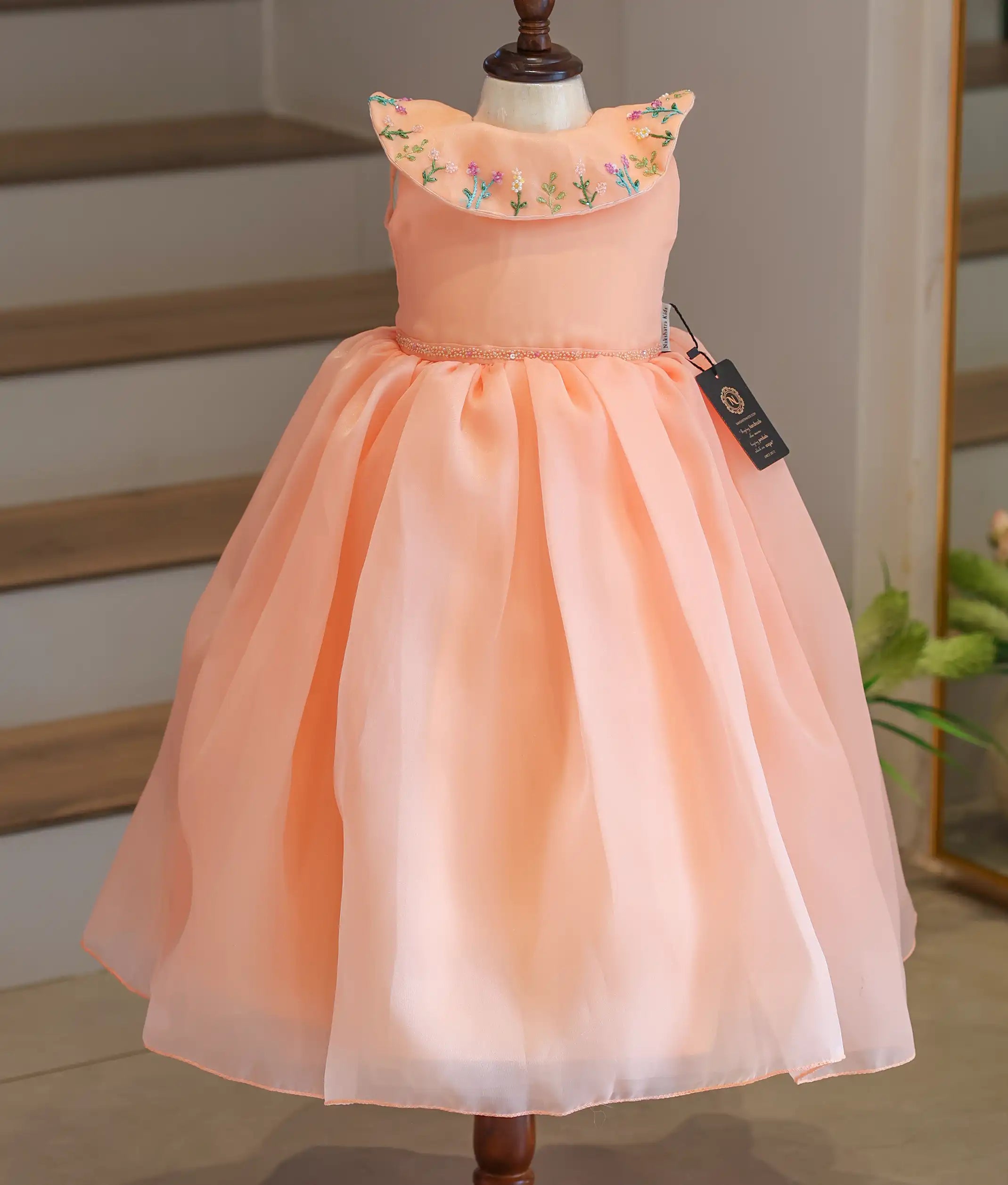 Front view of a peach girls' party frock featuring a floral embroidered Bertha collar.
