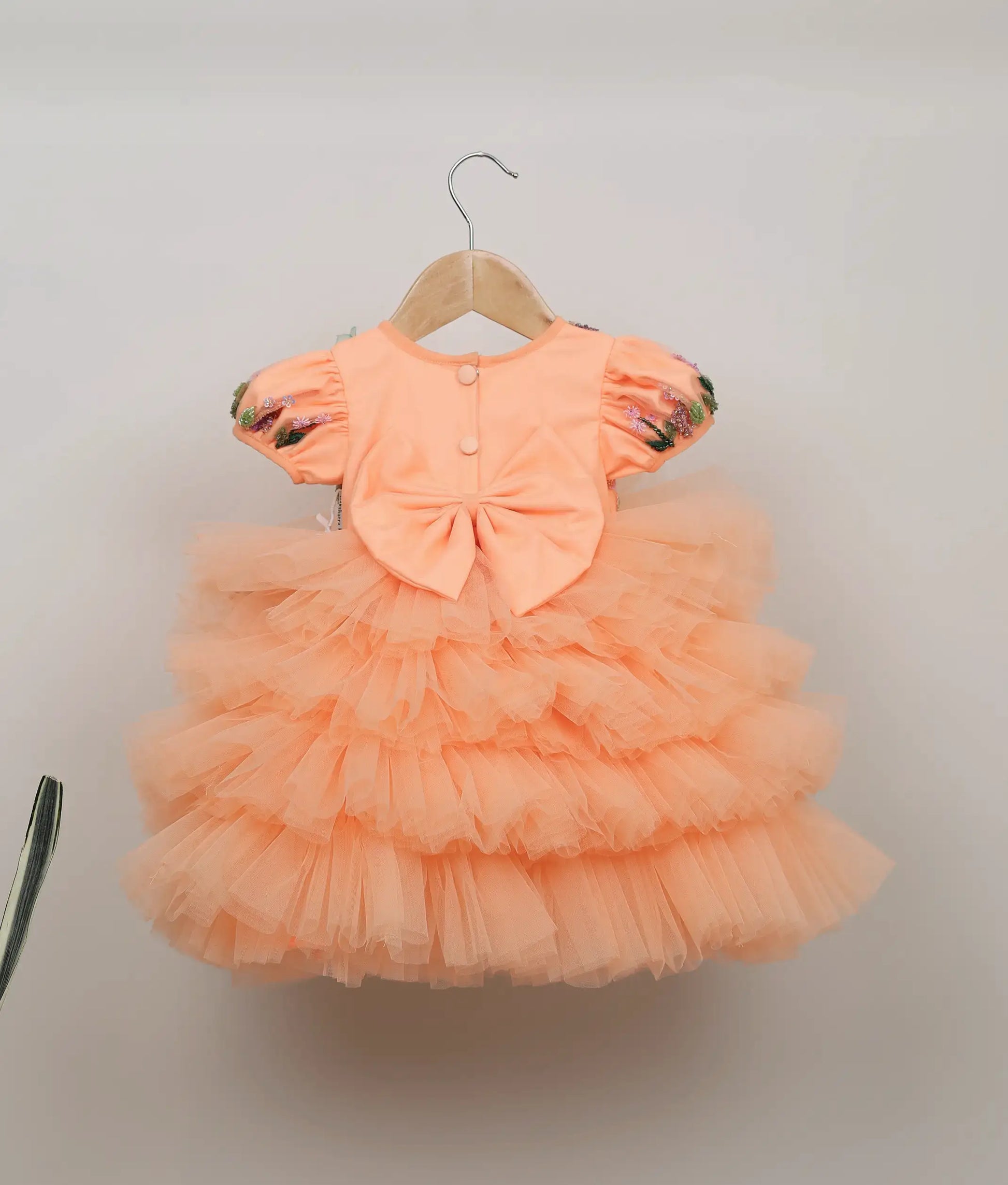 Back view of the peach butterfly theme dress showing the round neck, show button, and decorative bow
