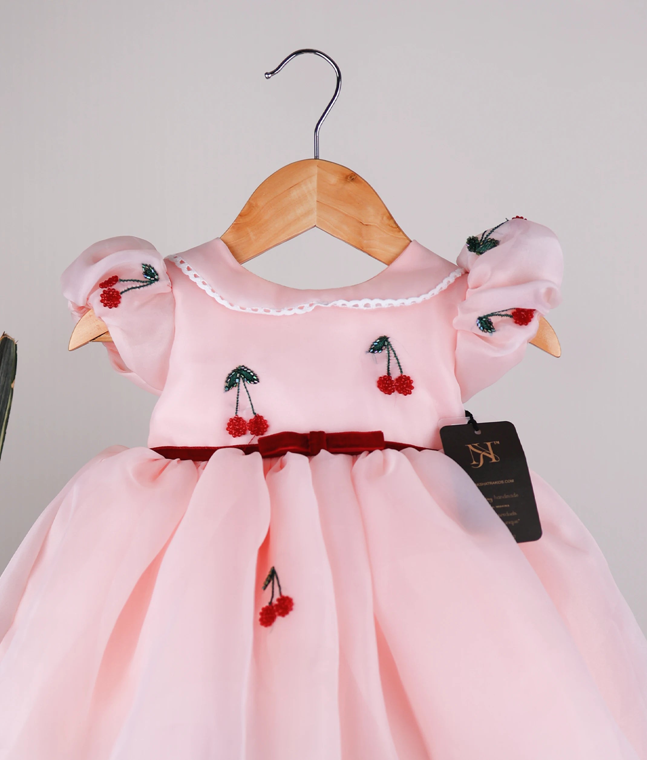 Close-up of the peach bodice showing handworked cherry motifs, a lace-trimmed Peter Pan collar, and a velvet waist ribbon