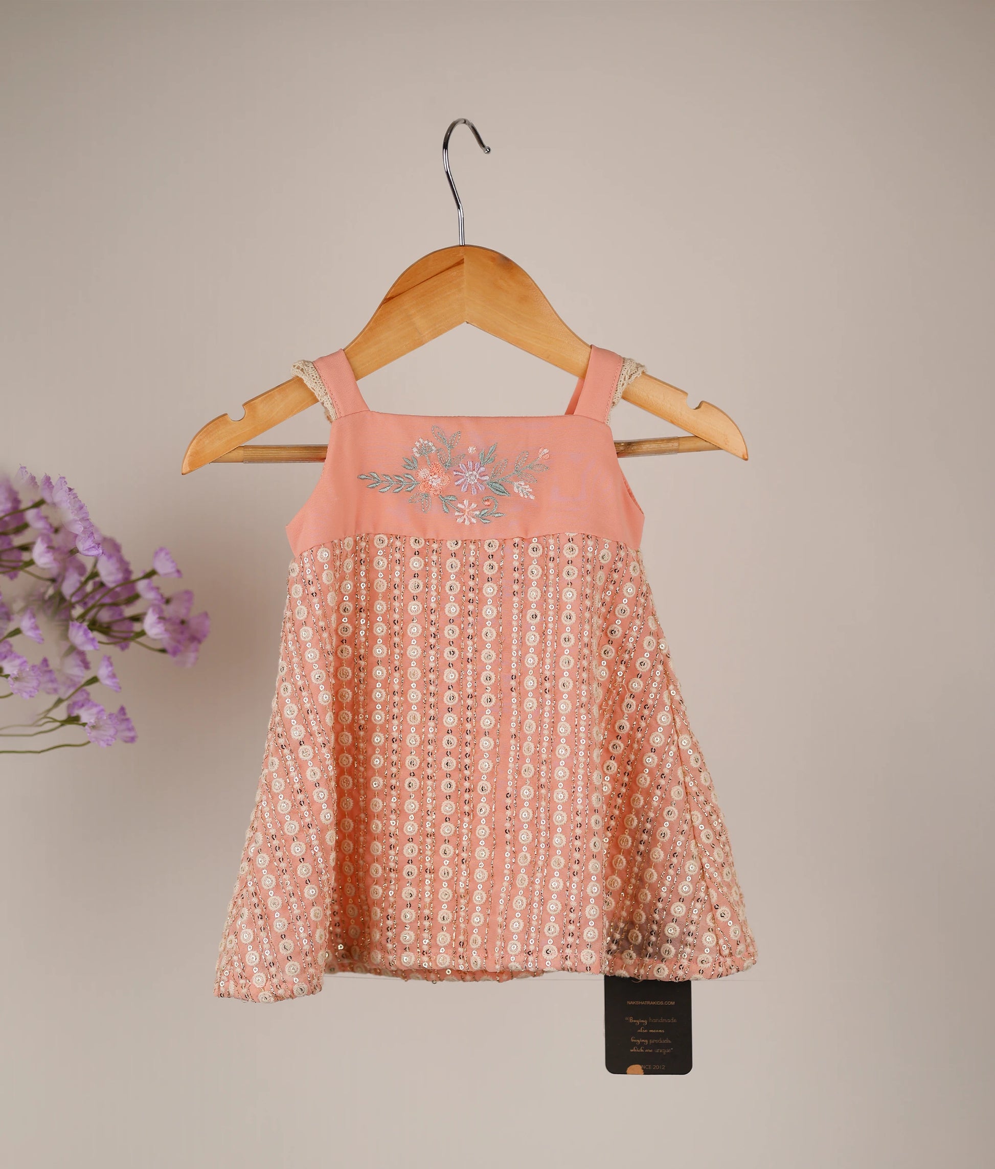Front view of a peach fancy material A-line frock for baby girls with machine embroidery