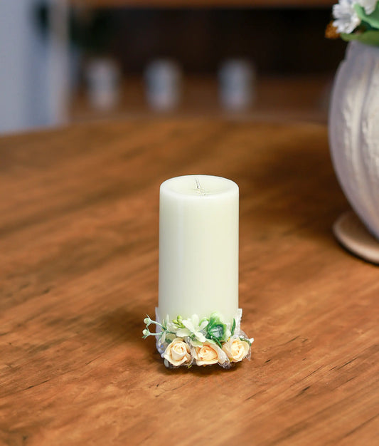Front view of a white baptism candle decorated with peach and cream flowers and a peach satin ribbon