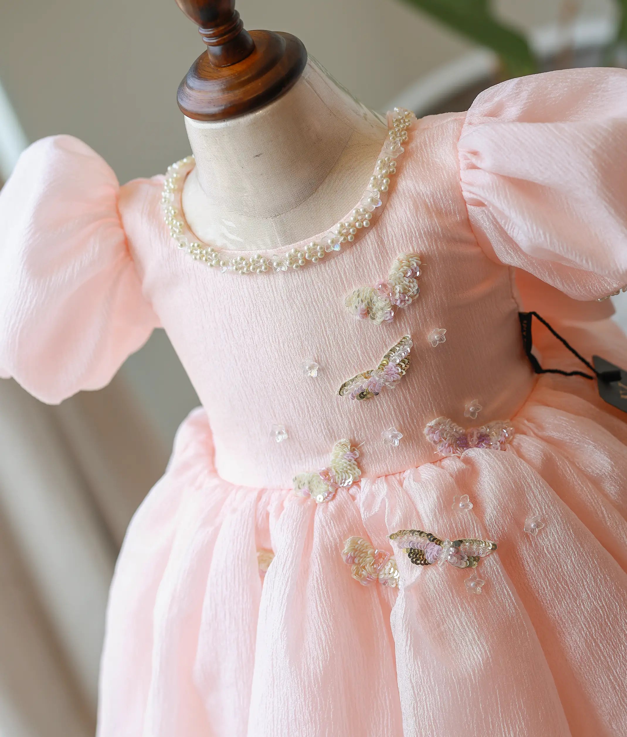 Close-up of the peach frock showing butterfly appliques, silver neckline trim, and pearl-trimmed puff sleeves
