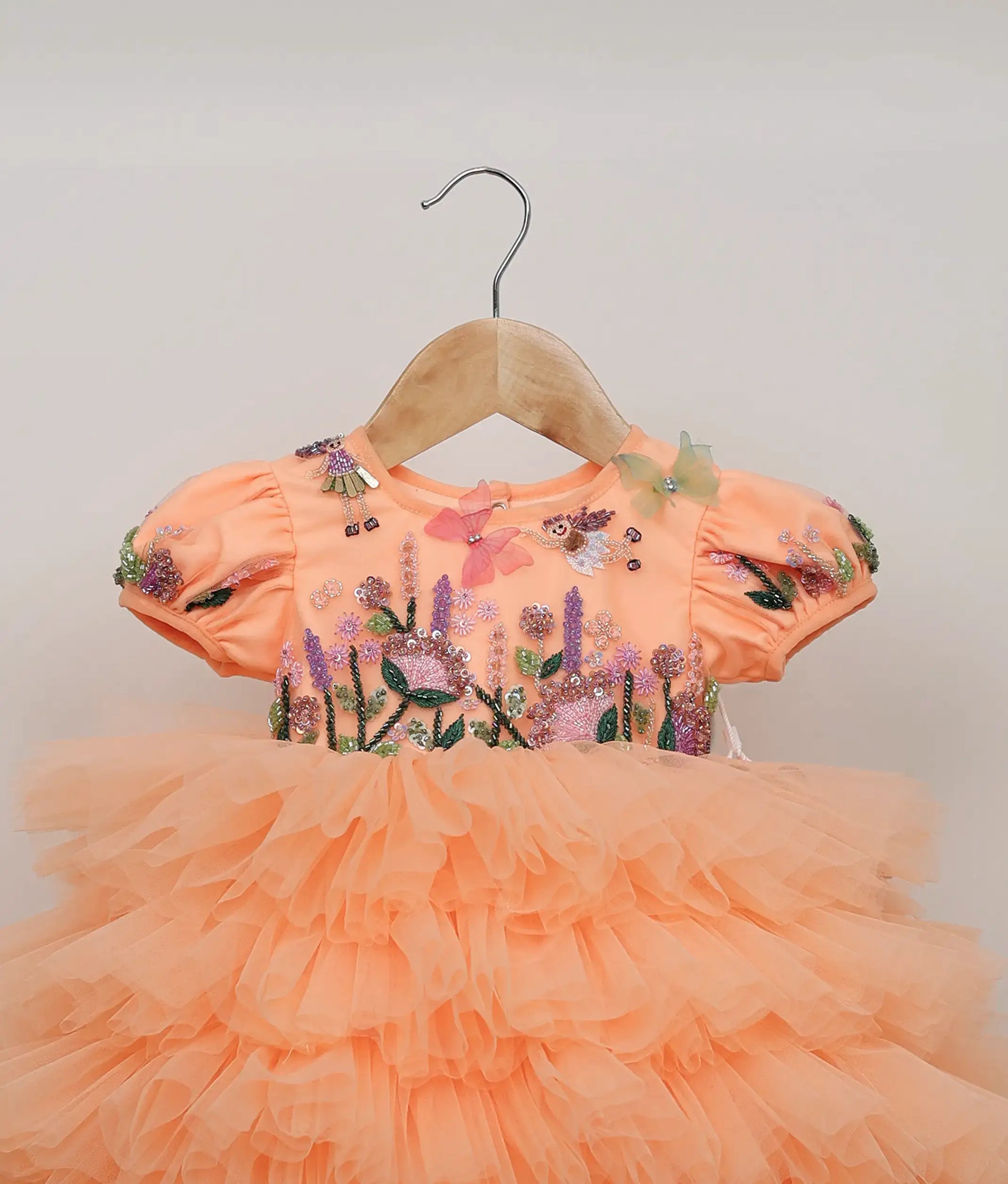 Close-up of the colorful butterfly and floral embroidery with sparkly sequins on the peach birthday frock