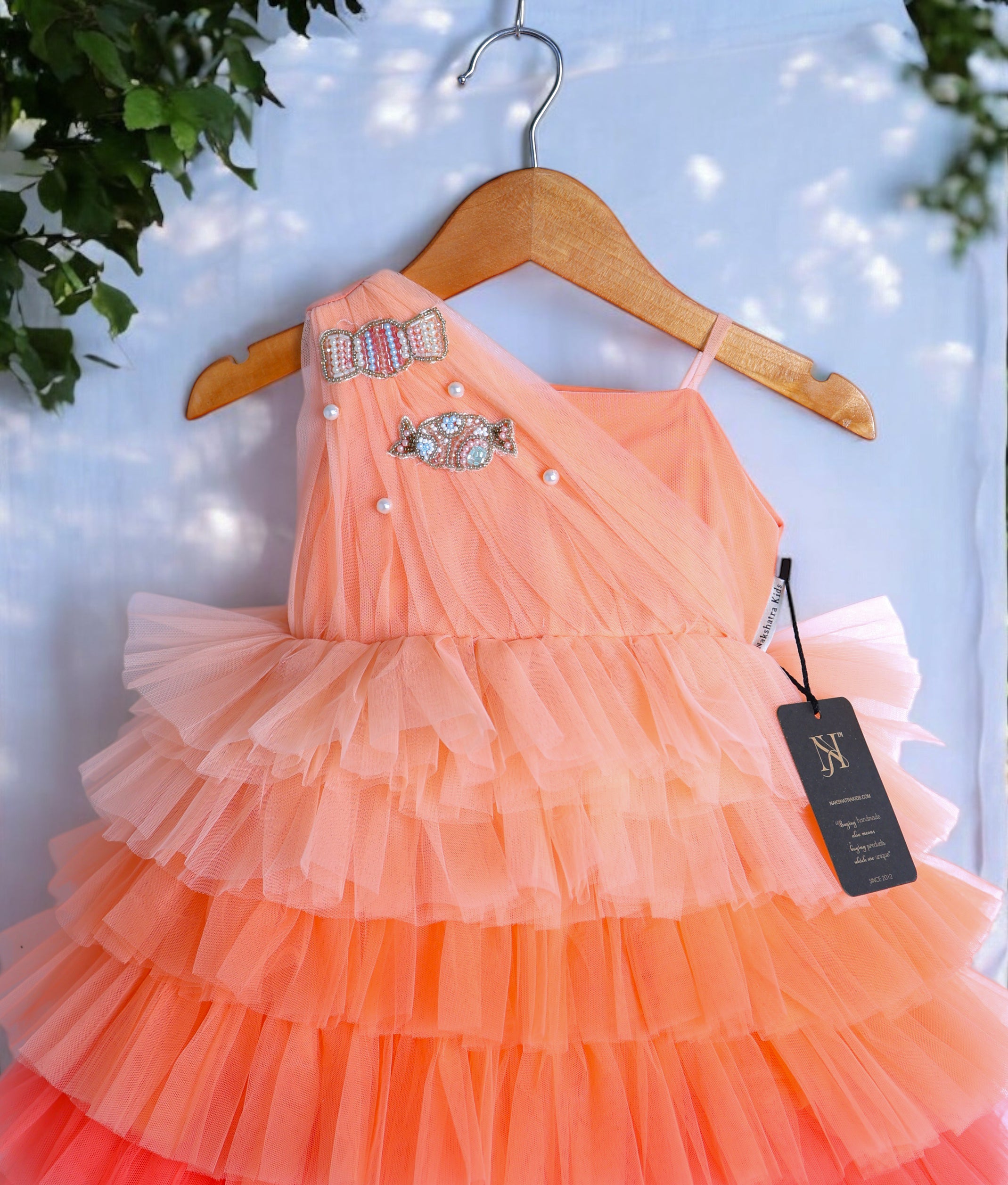 Close-up of the intricate candy-shaped pattern and pearl accents on the one-shoulder bodice of the peach birthday frock.