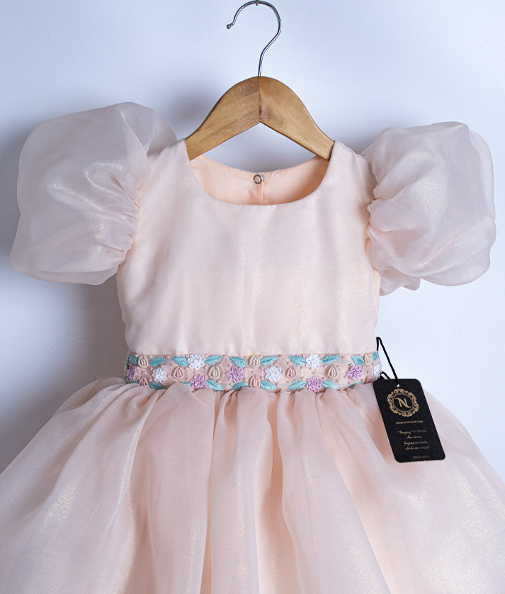 Close-up of the peach frock showing the pink and blue flower embroidery at the waist and balloon sleeve detail