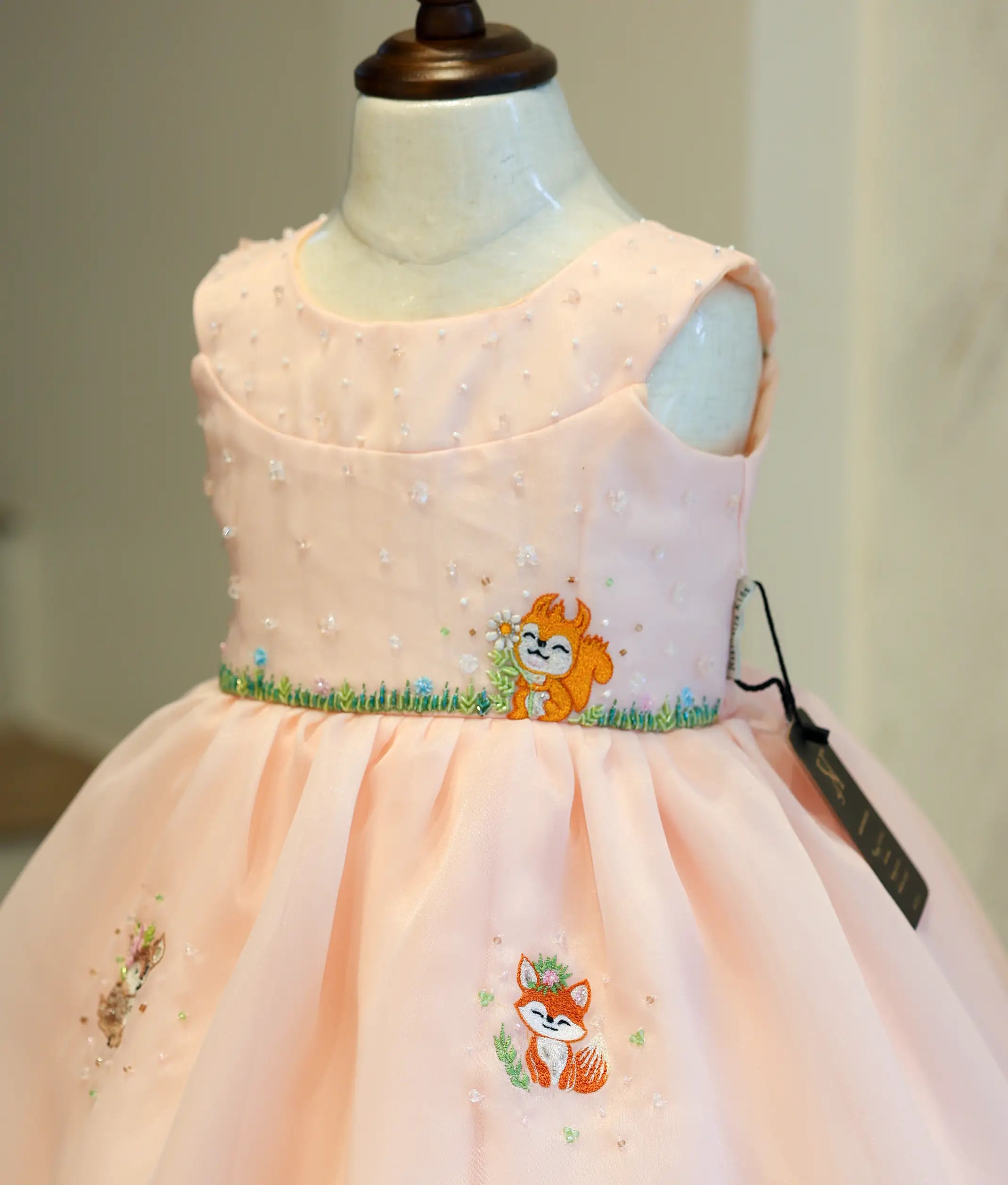 Close-up of the pastel peach frock bodice showing the embroidered fox motif and delicate pearl embellishments