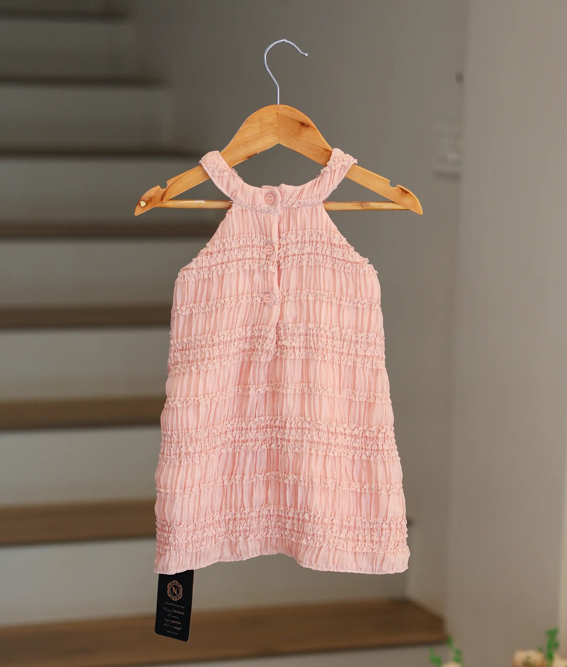 Back view of the peach georgette A-line frock highlighting the halter back and button closure.