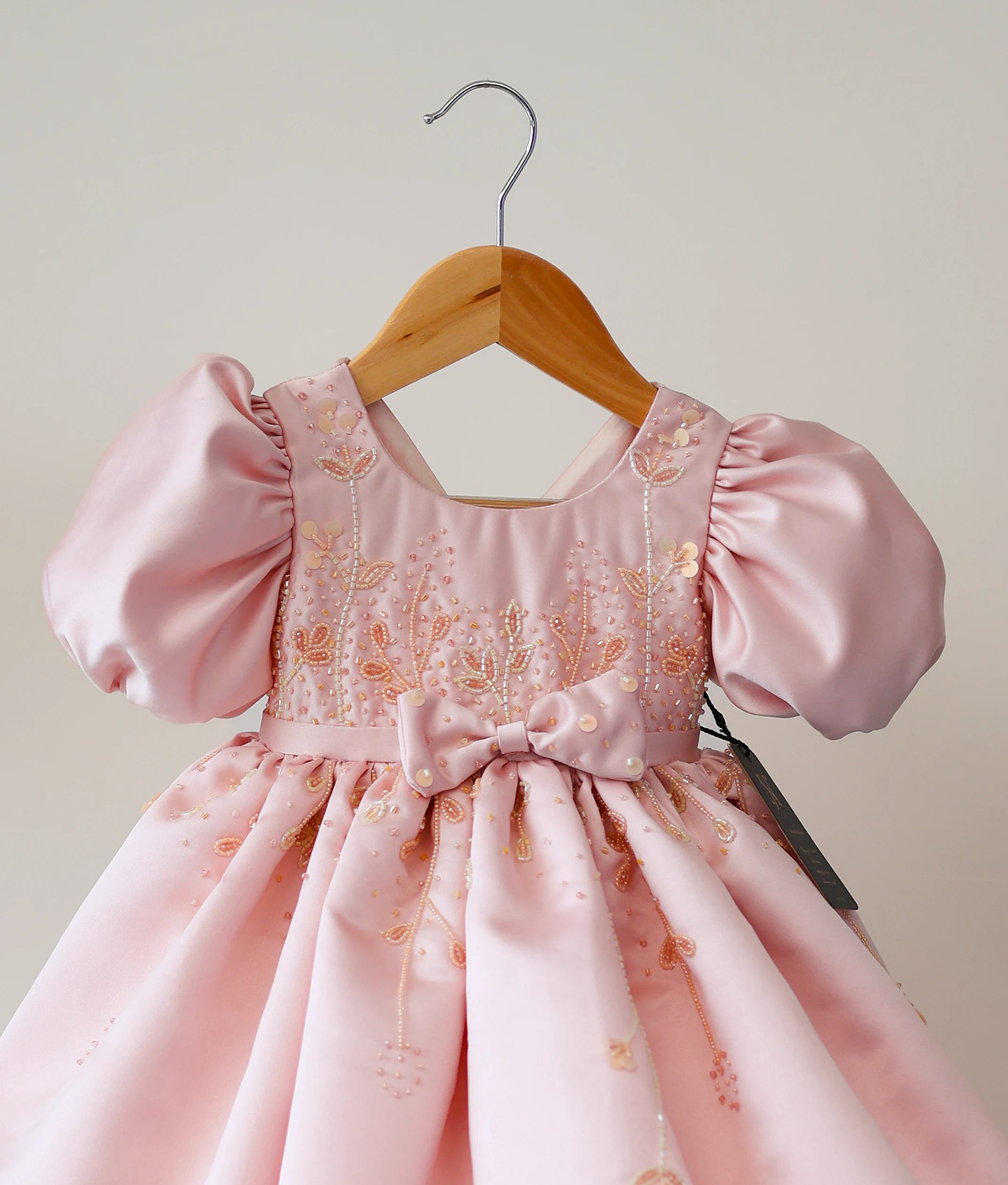 Close-up of the peach gown bodice showing the intricate cut-bead handwork, decorative bow, and balloon sleeve detail