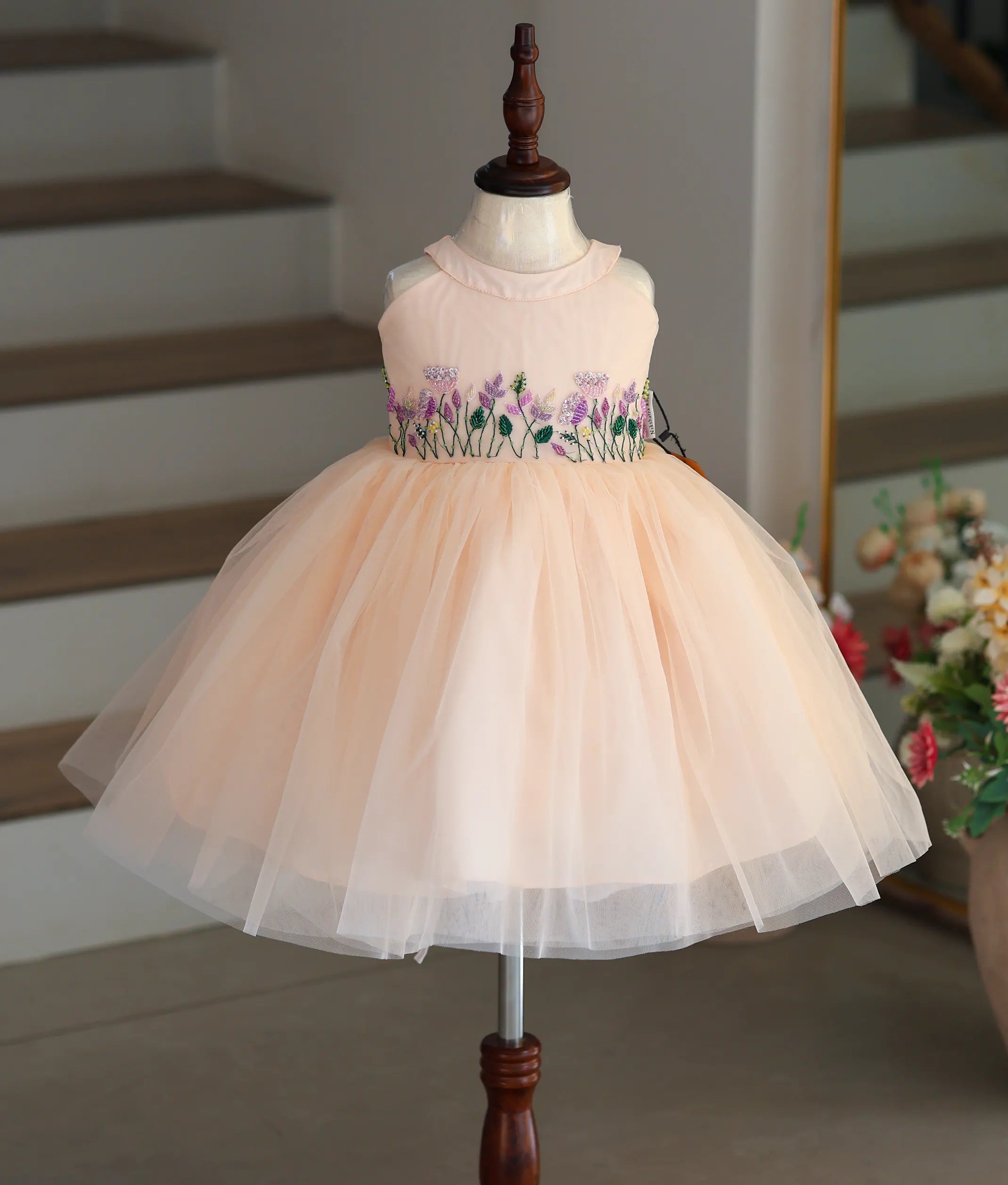 Full front view of a peach below-knee-length tulle net frock featuring a beaded halter neck and voluminous skirt.